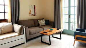 A living room with a sofa, a wooden coffee table, a blue chair, and a door with glass panels. - Emerald (Apokoronas)