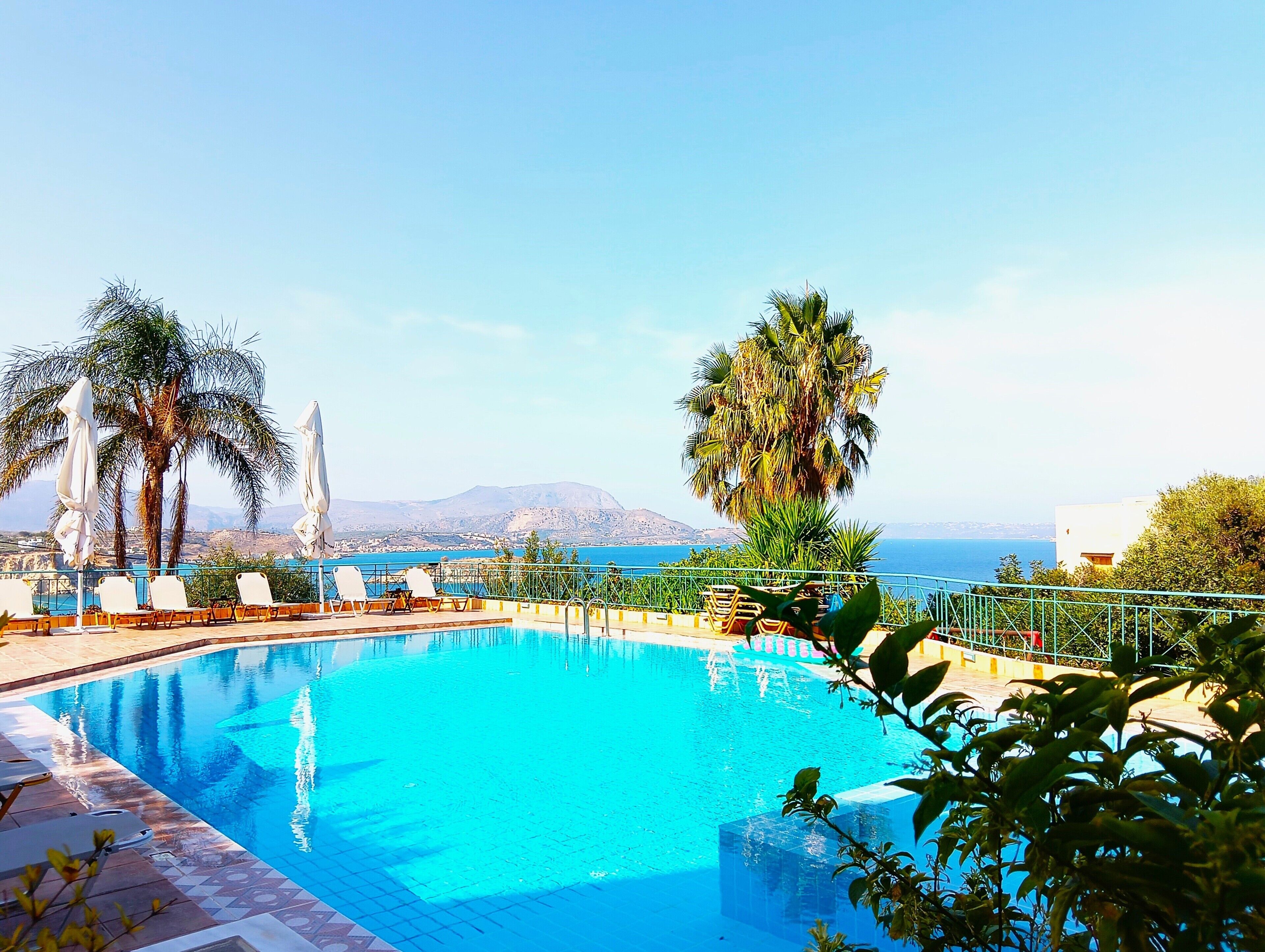 Une piscine avec des chaises longues, des palmiers et une vue sur la mer et les montagnes.