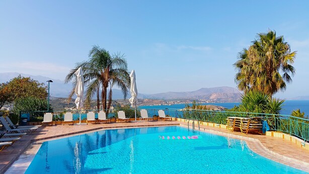 A clear blue pool with lounge chairs and umbrellas, surrounded by palm trees and a view of the sea and mountains. - Emerald (Apokoronas)