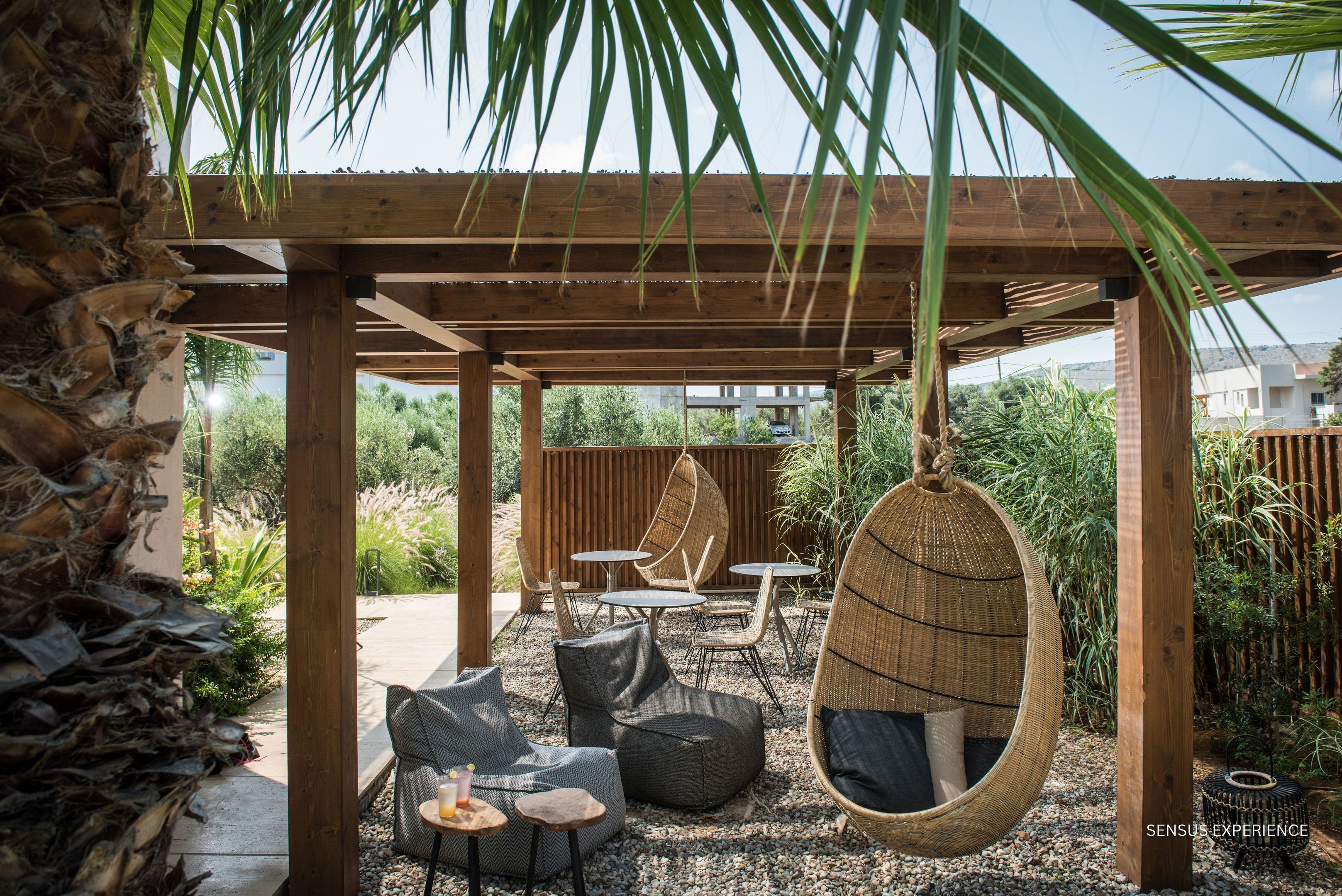 An outdoor patio with wooden pergola, hanging chairs, and a seating area with cushions and tables.