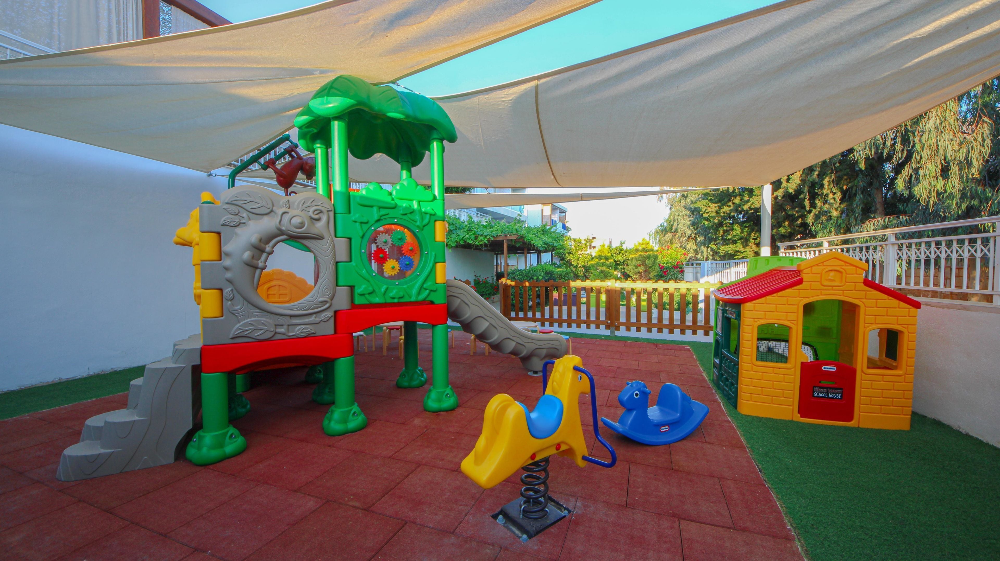 A children's play area with a slide, climbing structures, and a small house.