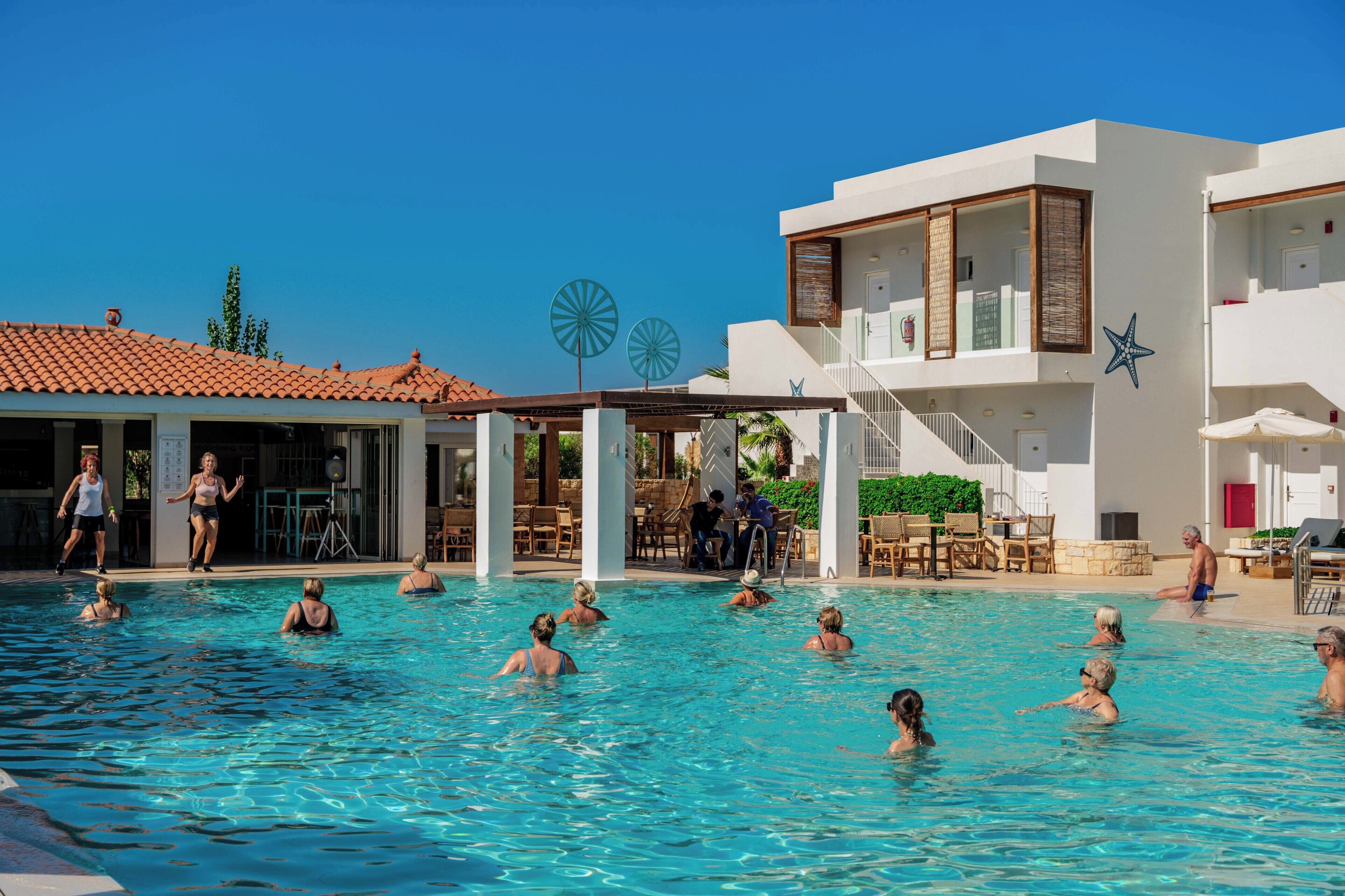 A swimming pool area with multiple levels of buildings, including a covered patio and a poolside lounge.