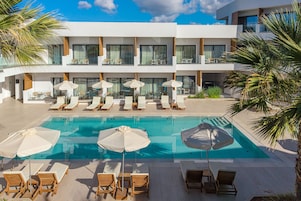 A modern hotel with a pool area, multiple lounge chairs, and umbrellas.
