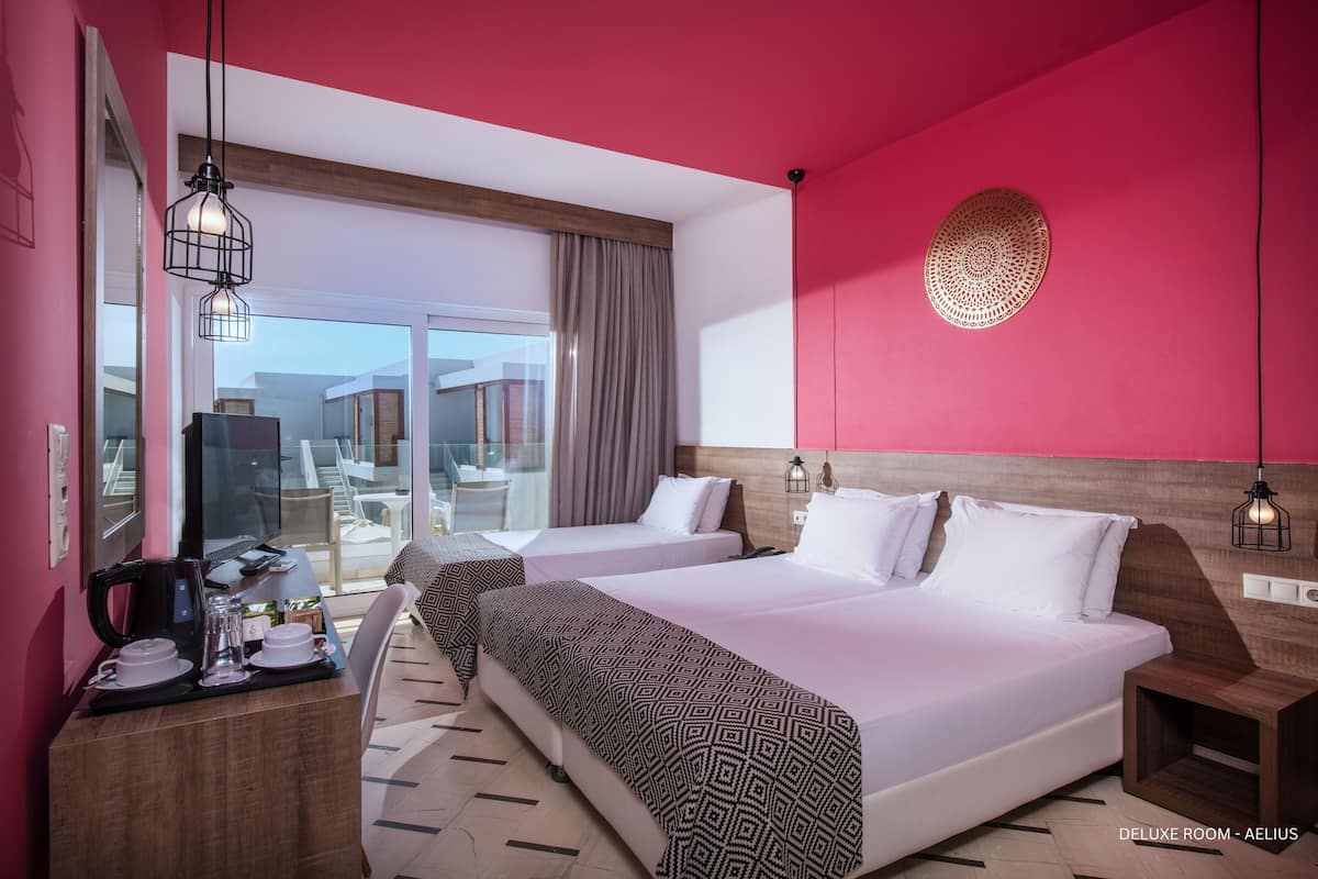 A room with two beds, a desk with a coffee maker, and a large window.