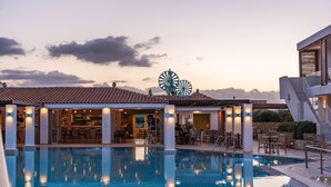 Una piscina con zona de bar y asientos al aire libre, rodeada de edificios con tejados de cerámica.