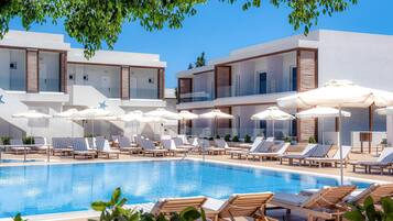 A pool area with multiple lounge chairs and umbrellas, surrounded by modern buildings with balconies.