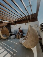 A modern outdoor seating area with hanging chairs, a sofa, and a small table with a drink.