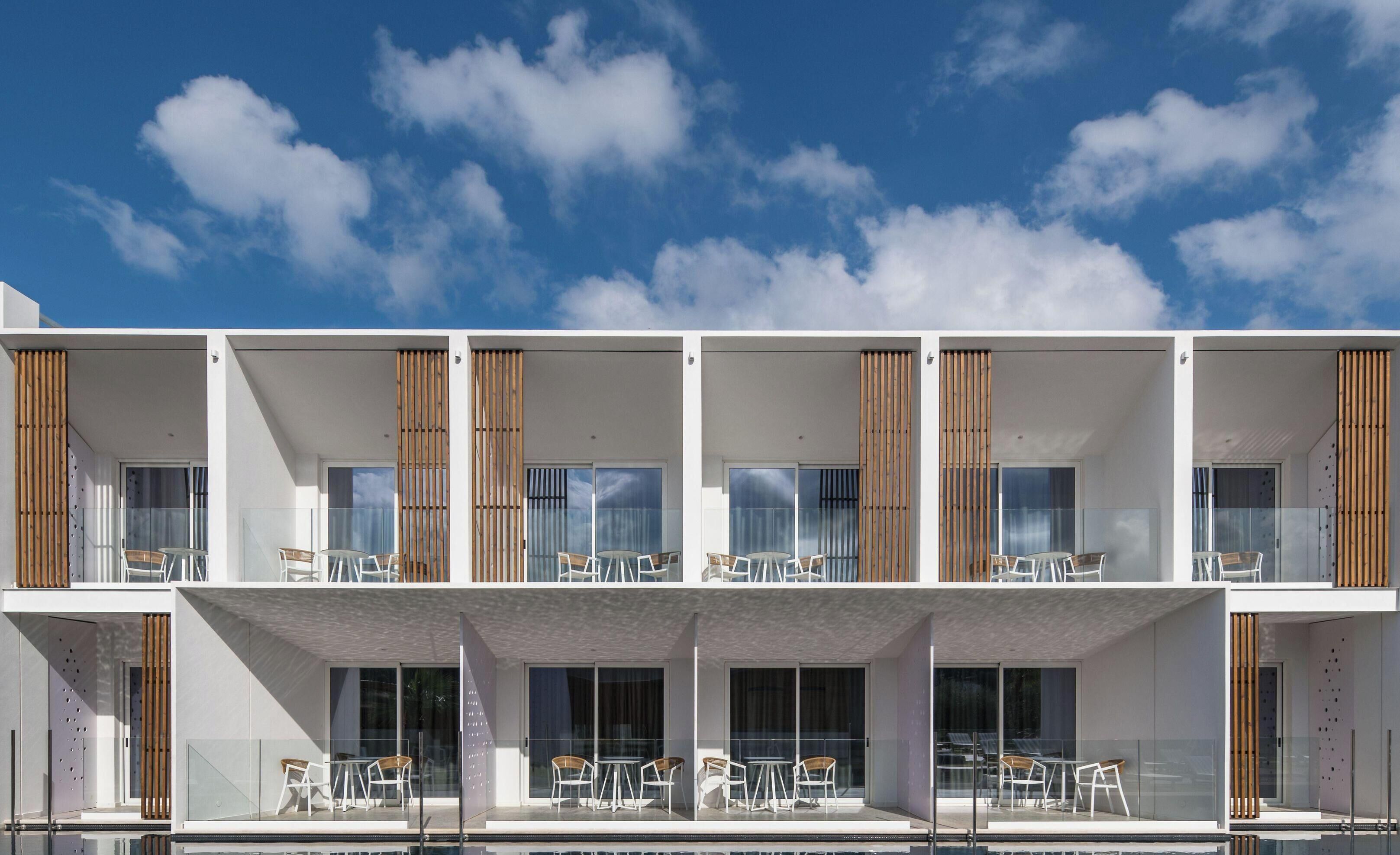 A modern multi-story building with balconies, glass doors, and outdoor seating areas.