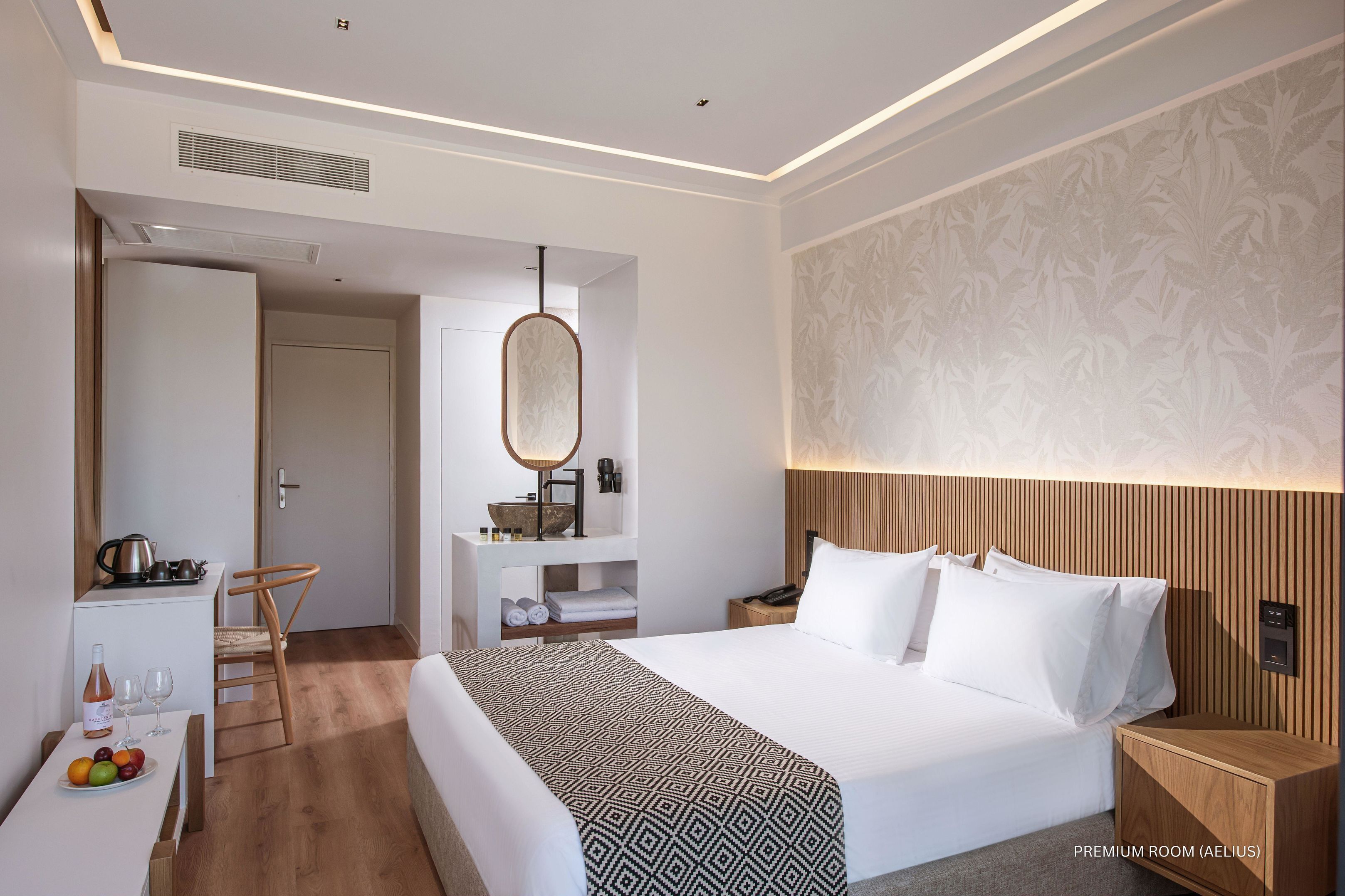 Une chambre d’hôtel bien éclairée, dotée d’un grand lit, d’une table de chevet, d’une commode, d’une armoire, d’un miroir et d’un petit coin cuisine.