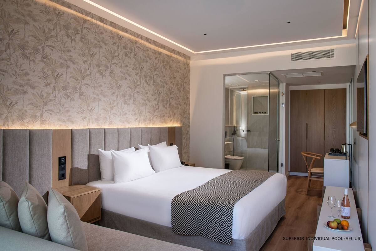 A modern hotel room with a large bed, a bedside table, a small desk, and a seating area.