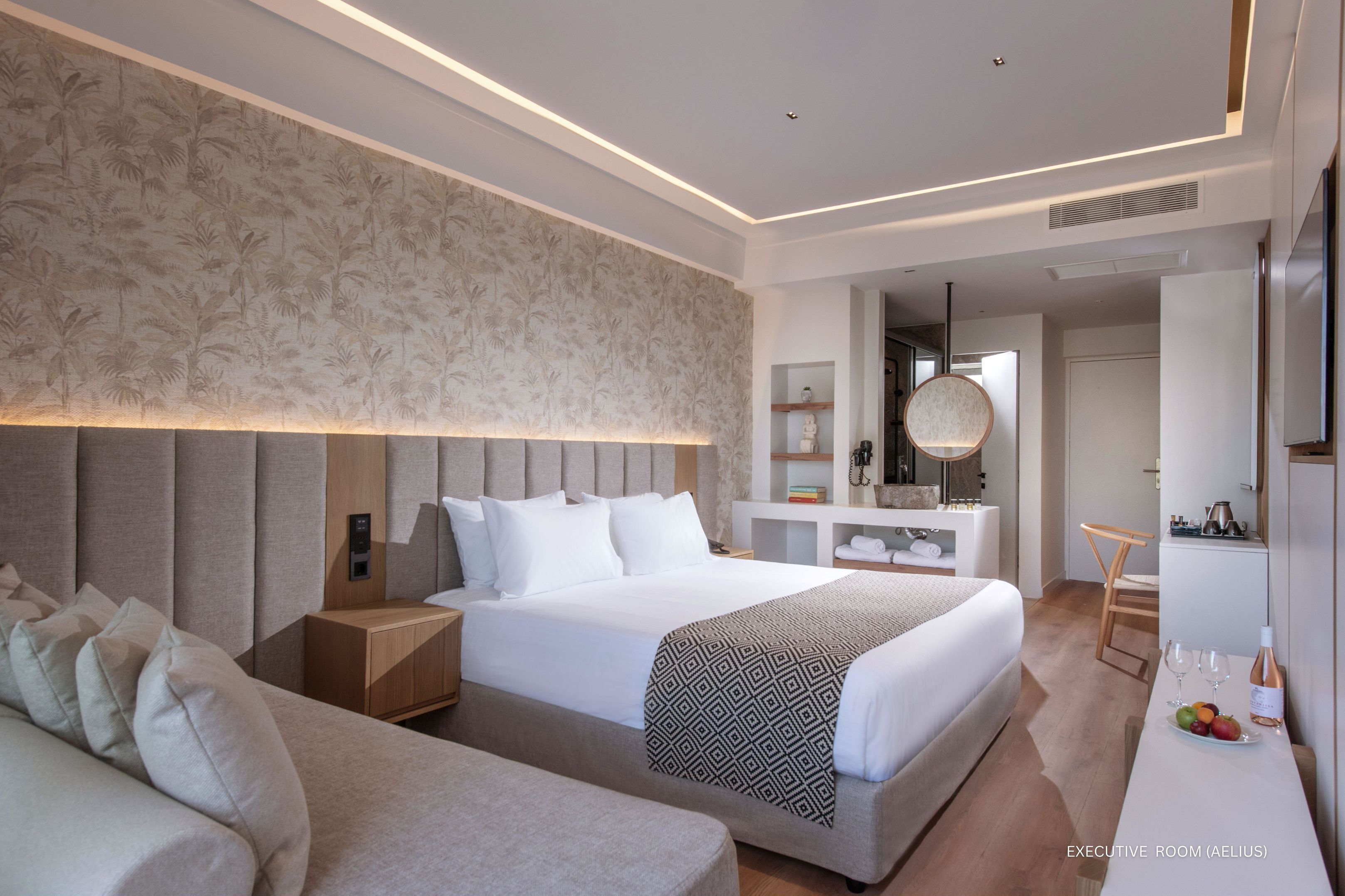 A modern executive room with a large bed, bedside tables, a desk, and a seating area.
