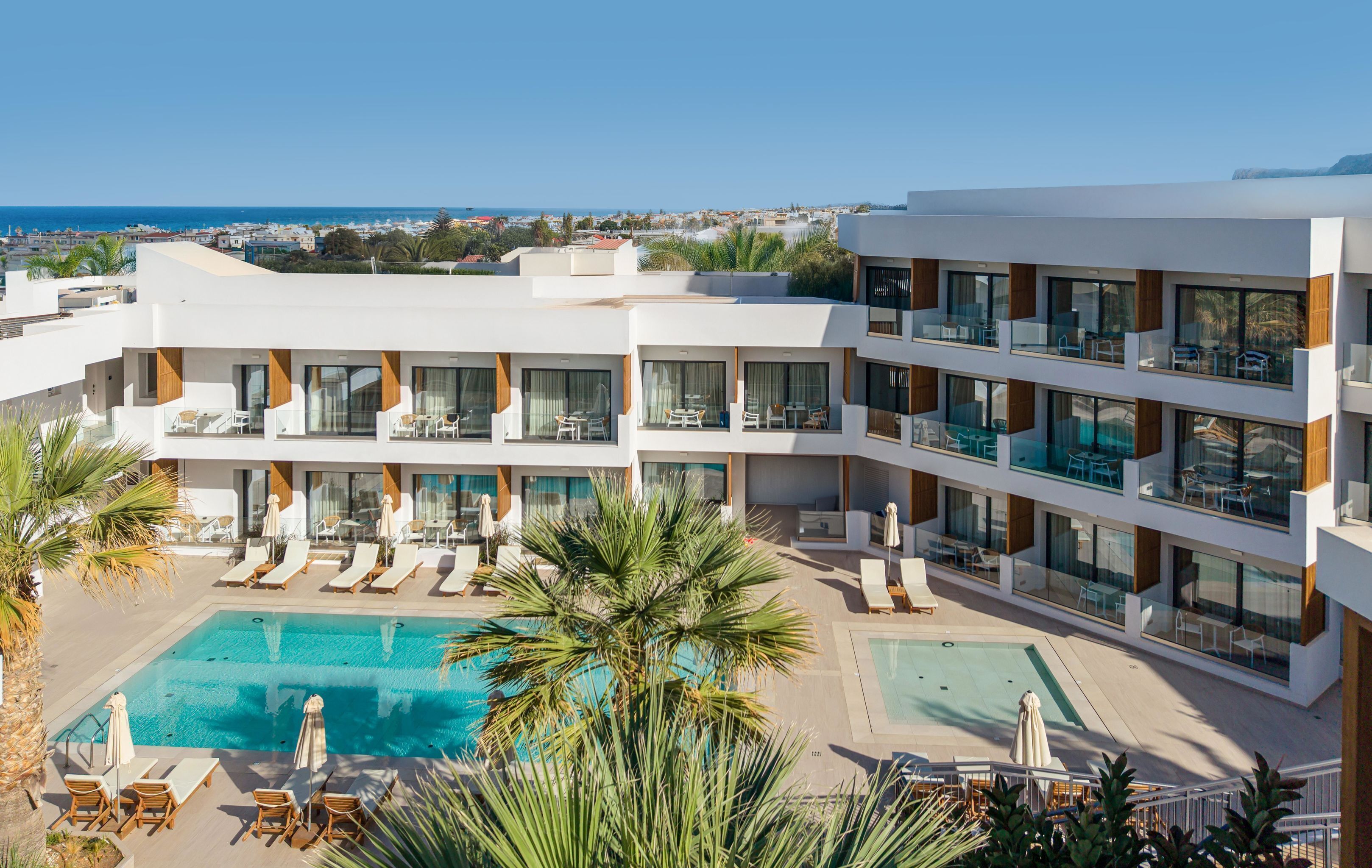 Een modern hotel met een zwembad, meerdere balkons en uitzicht op zee.