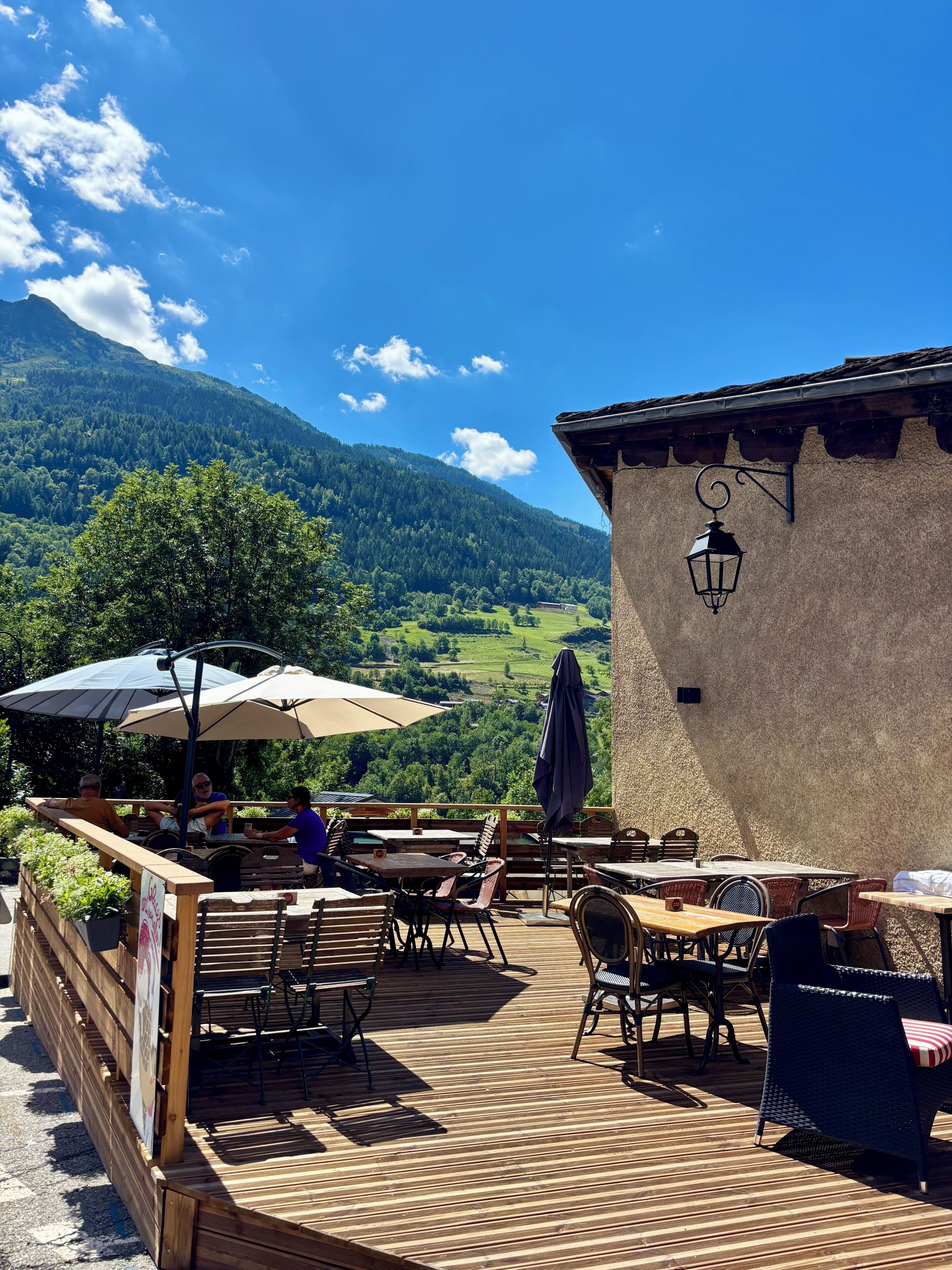Un espacio al aire libre con mesas y sillas, una terraza de madera y vistas a la montaña.