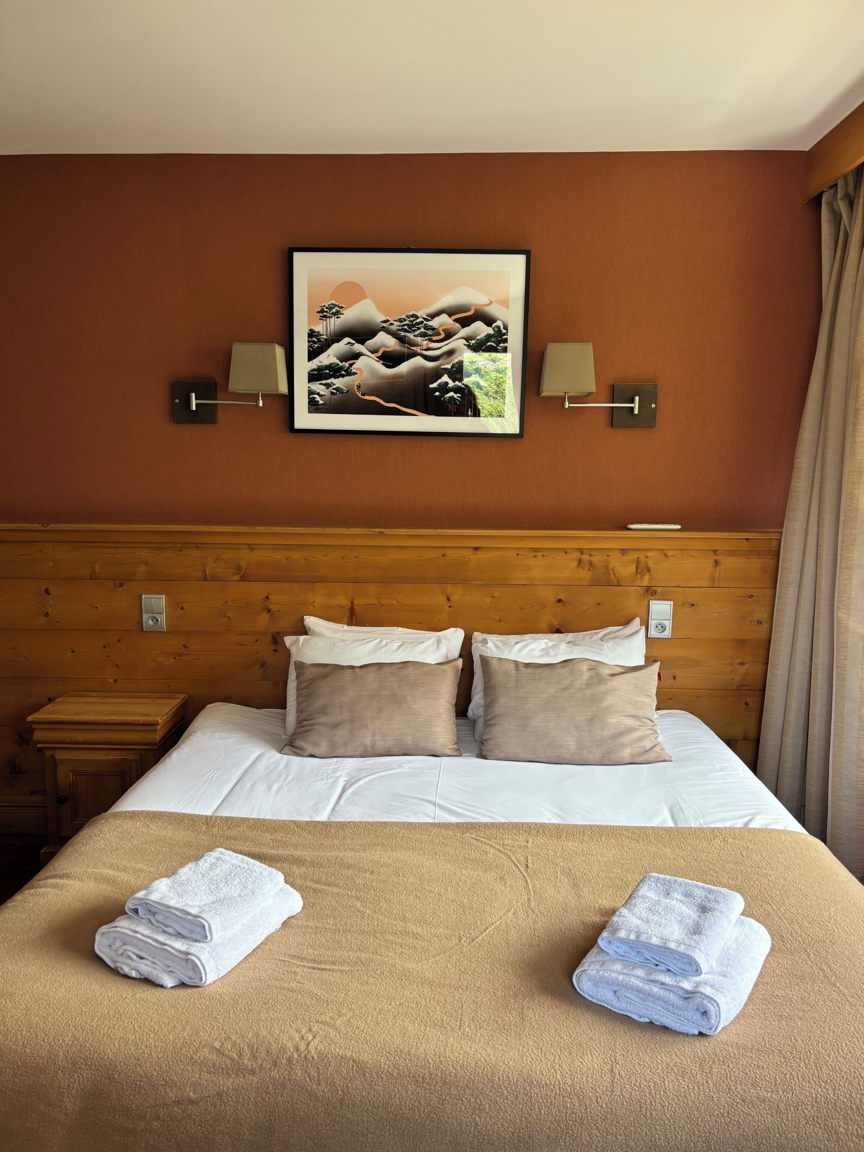 A neatly made bed with two pillows, a framed picture on the wall, and two bedside lamps.