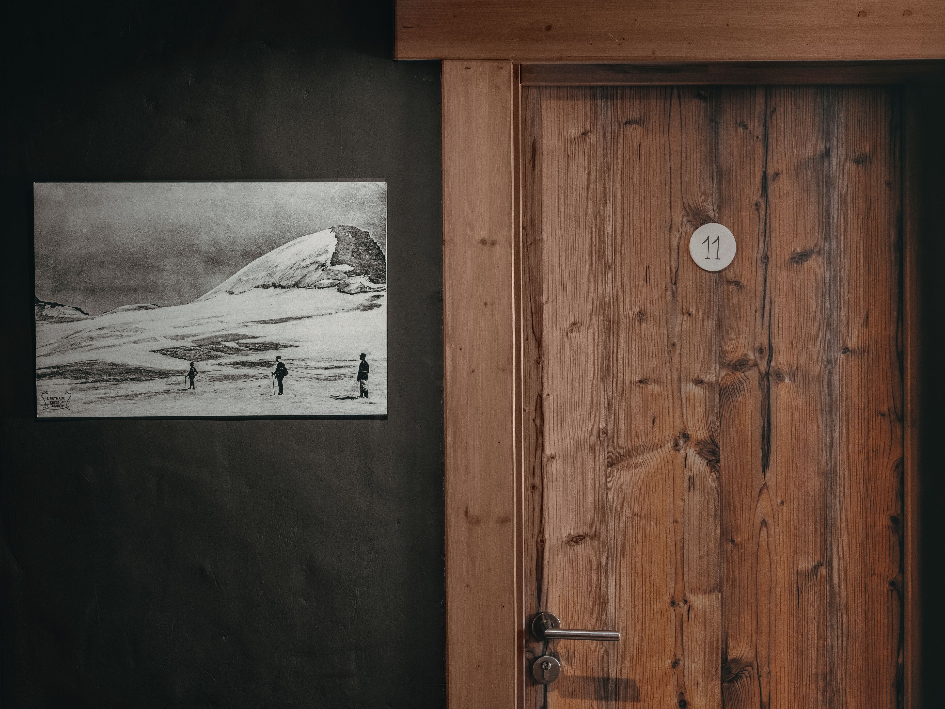 Una puerta de madera con una placa de número y una fotografía blanco y negro de un paisaje nevado con gente.