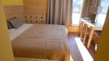 Een slaapkamer met een groot bed, een houten hoofdbord, een bureau met stoelen en een raam met gordijnen.
