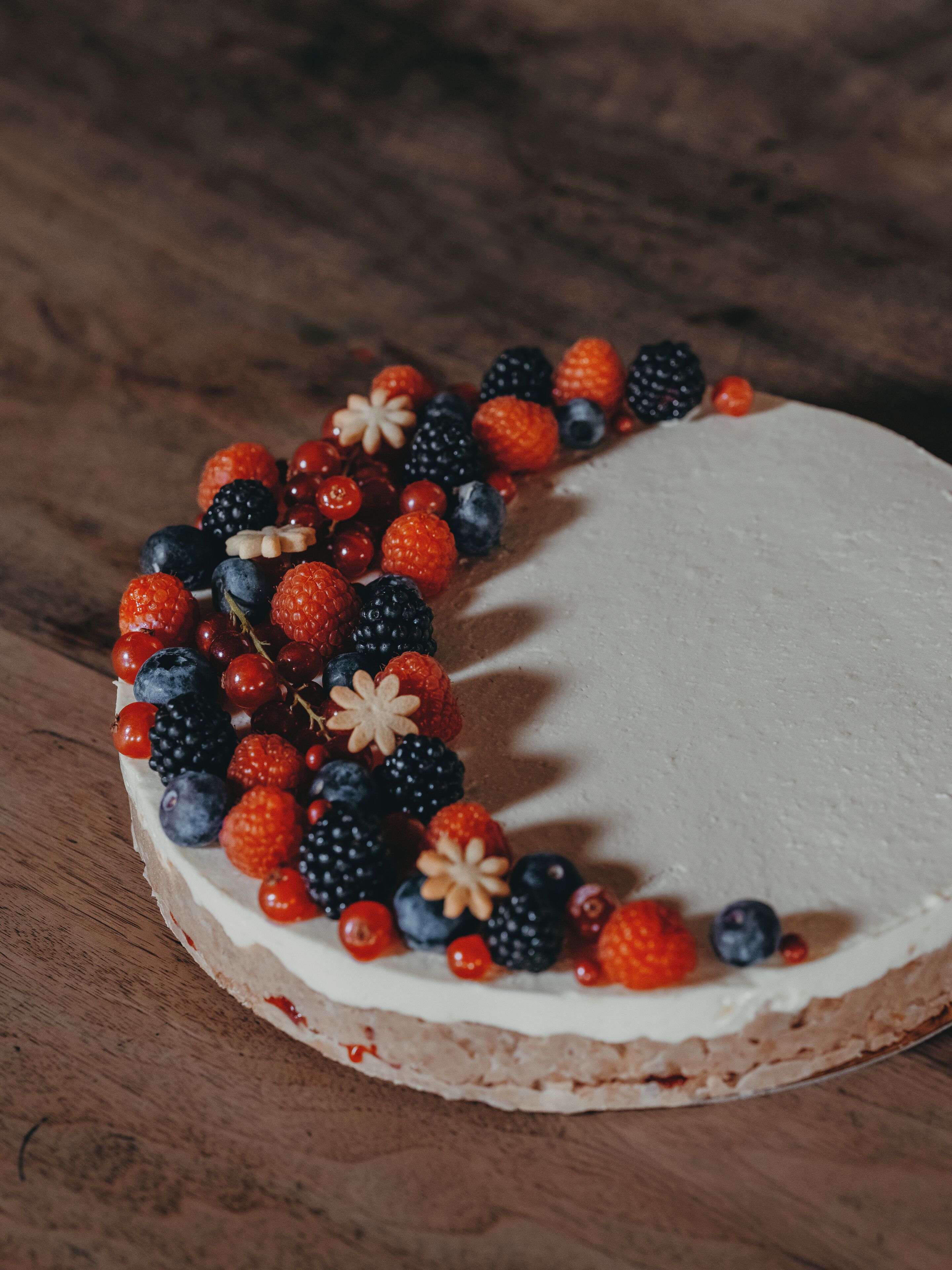 Un pastel redondo con base de crema blanca, decorado con diversas bayas y una flor encima.