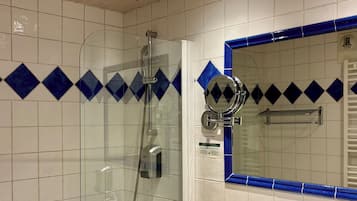 Un baño con ducha envuelta en vidrio, techo de madera, lavamanos blanco con encimera de madera y espejo con marco de azulejos azules.