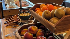 A breakfast buffet with fruits, a coffee station, and a view of a mountainous landscape.