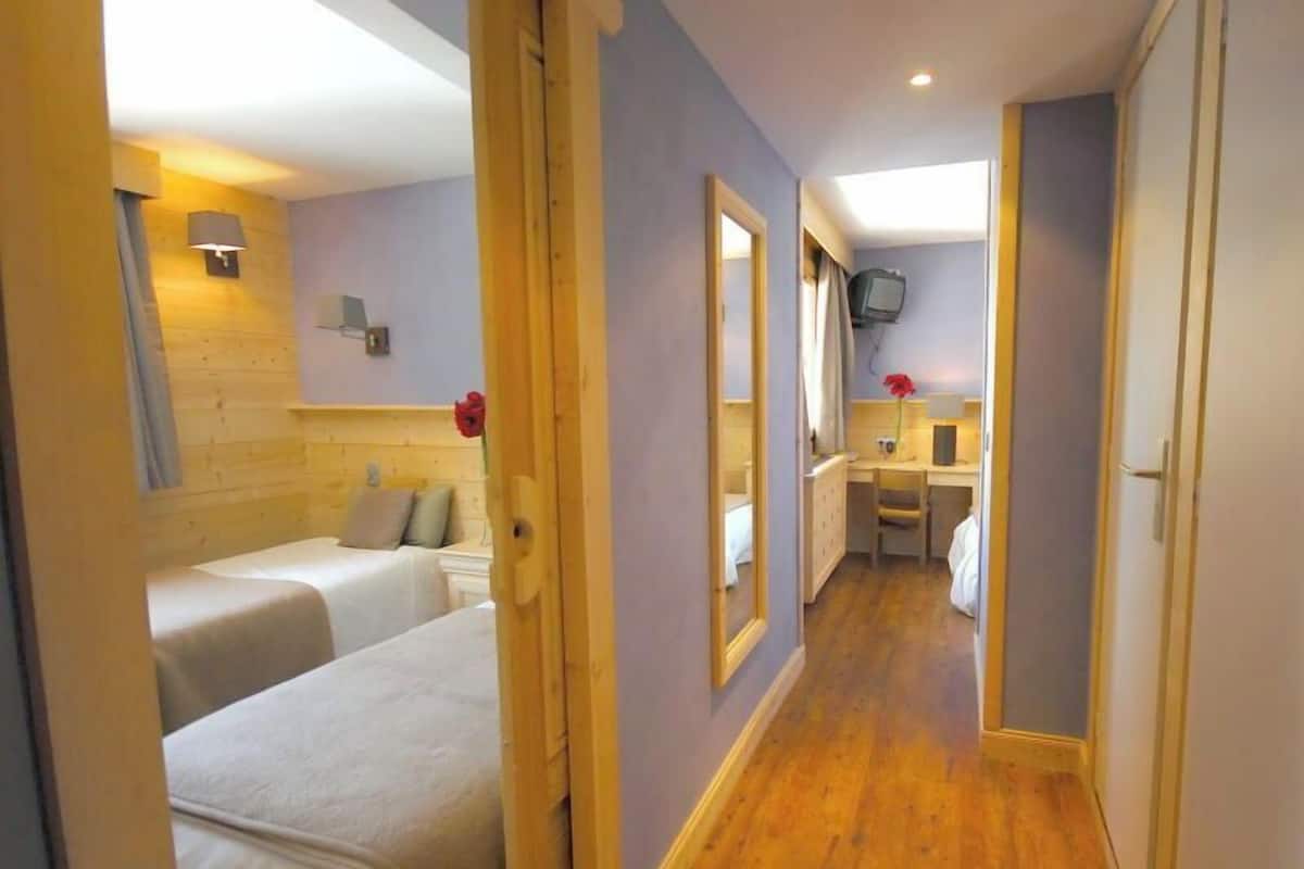 A hotel room with two beds, a desk, a mirror, and a television.