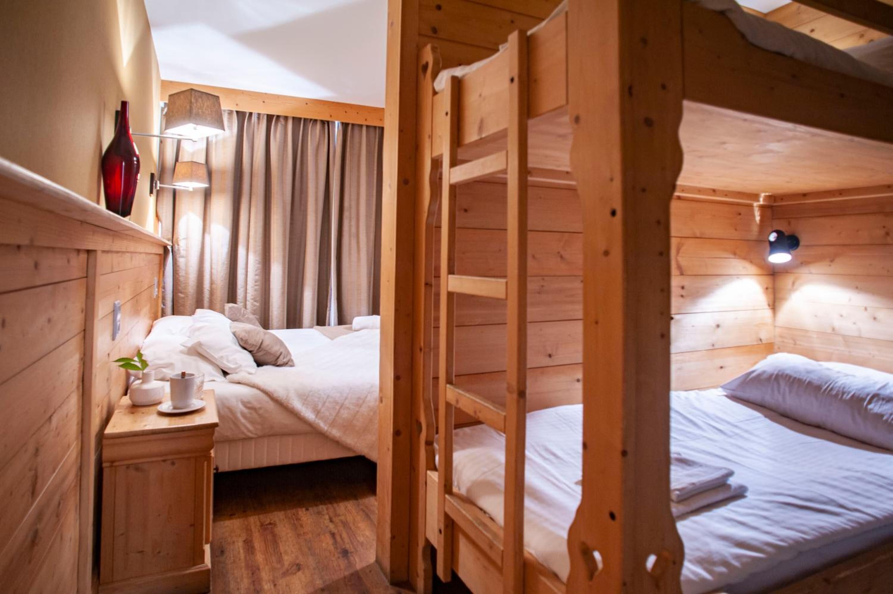 Una habitación tipo cabaña de madera con literas, una mesita de noche con lámpara y una ventana con cortinas.