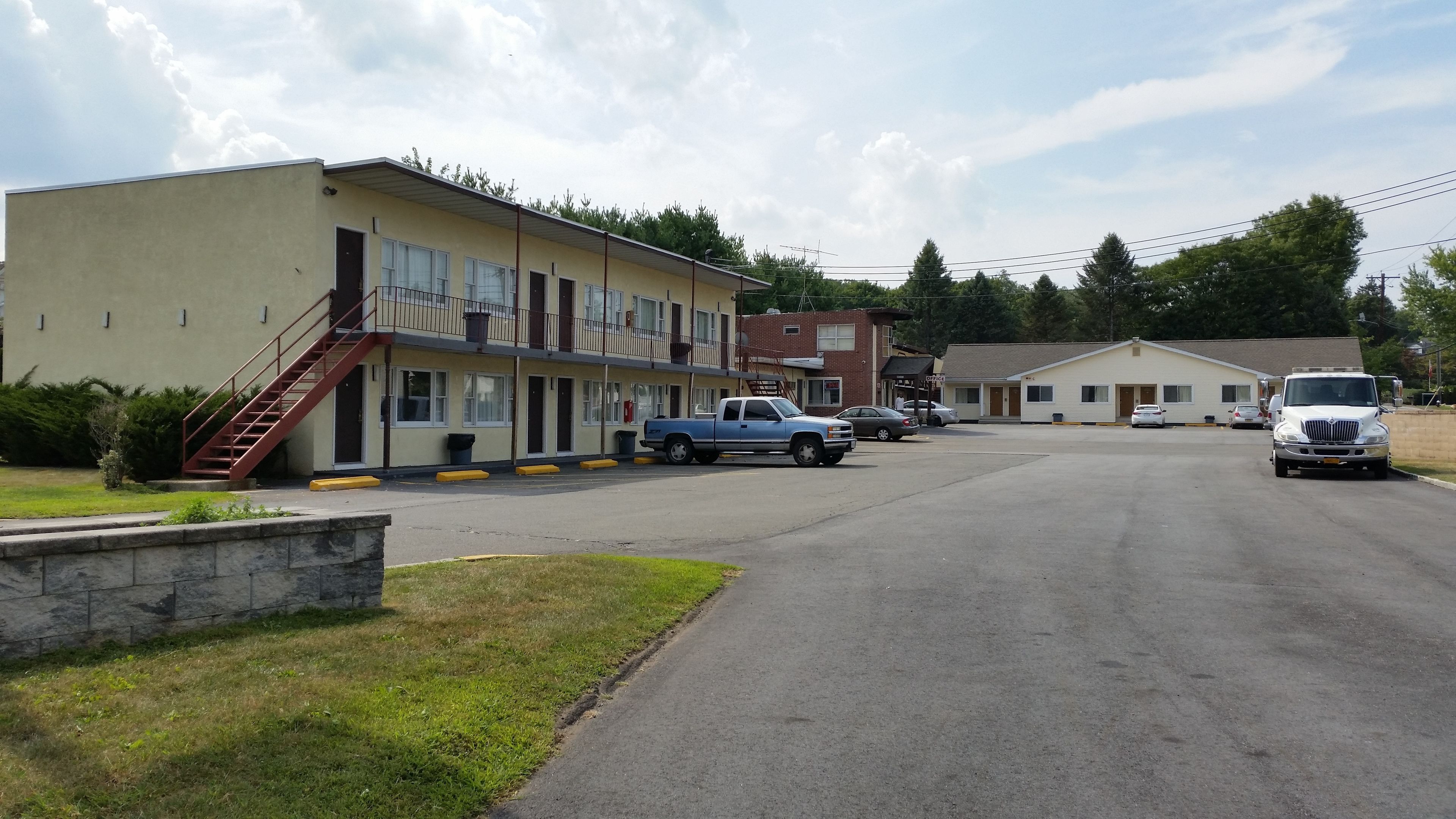 A motel with a two-story building, a covered parking area, and a large truck parked in the lot.