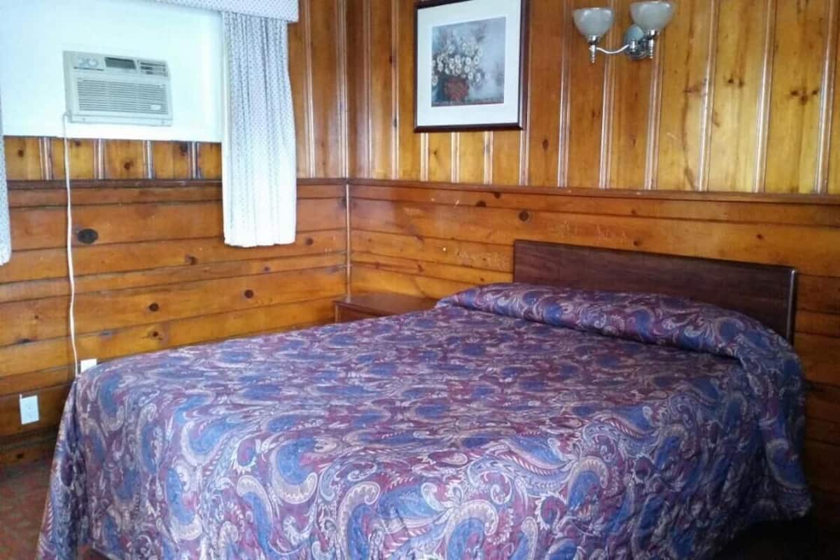 A wooden-paneled room with a bed, a picture on the wall, and a window with curtains.