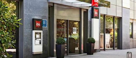 Entrada moderna de un hotel con un cartel de 'ibis Barcelona Mallet' y un símbolo de accesibilidad para sillas de ruedas.