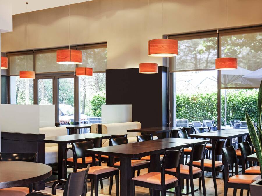 Un comedor moderno con mesas y sillas, ventanas amplias y lámparas colgantes.