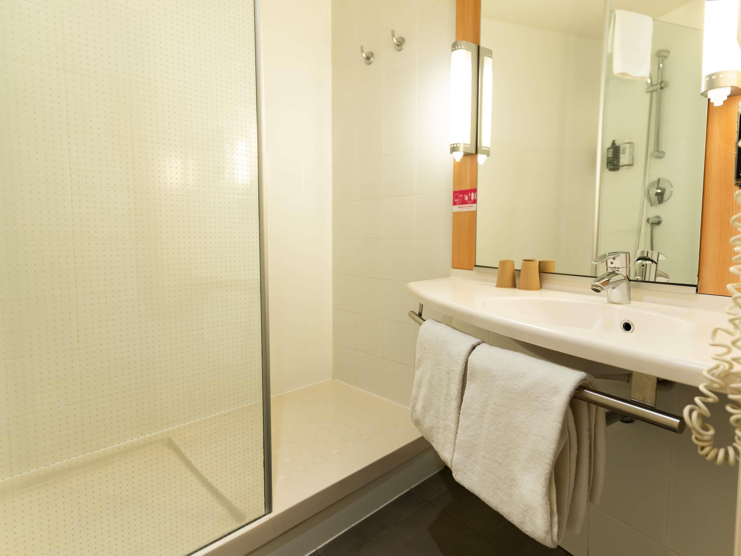 Un baño con cabina de ducha de vidrio, un lavabo blanco con espejo y un perchero para toallas.