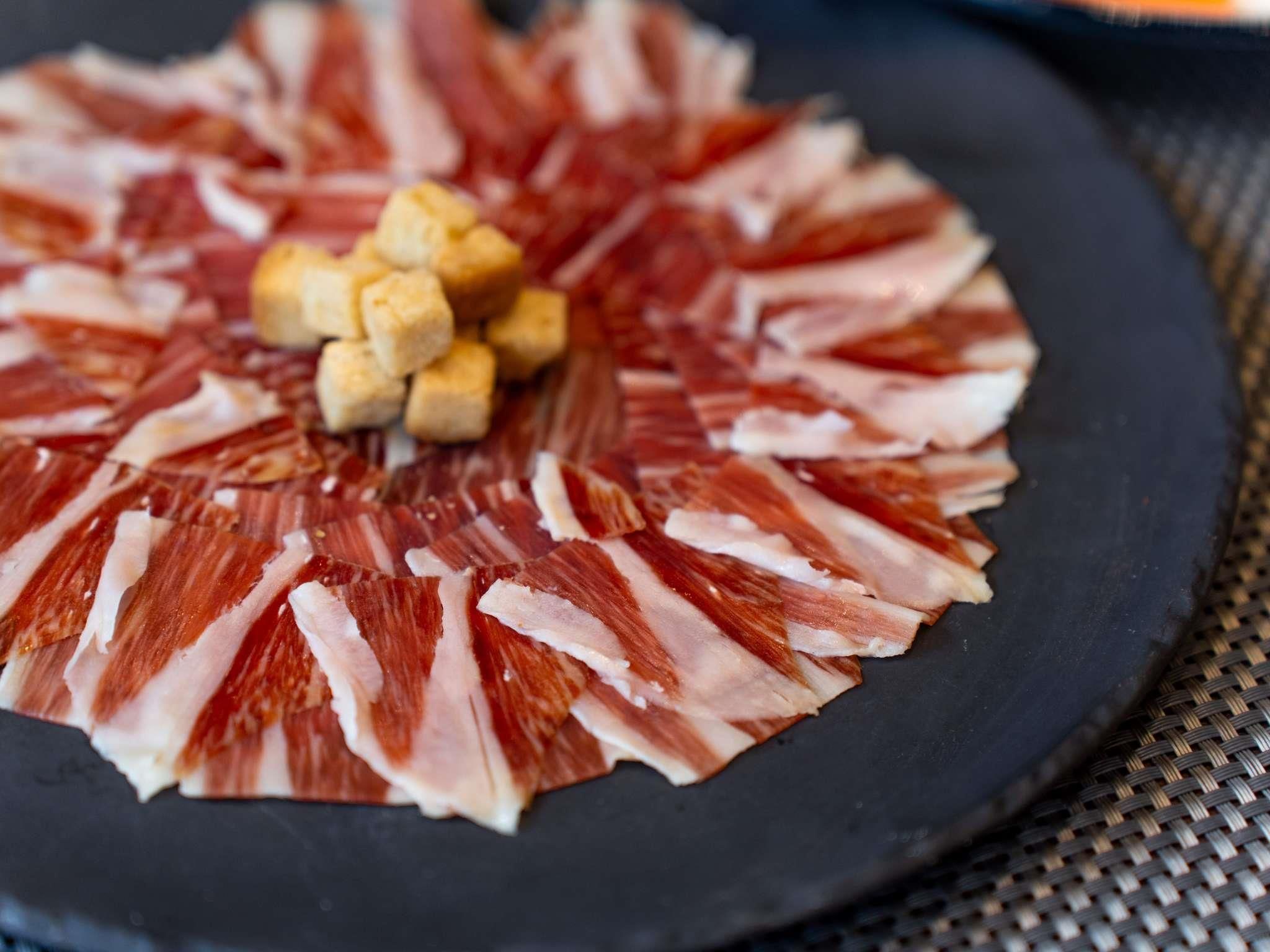 A circular arrangement of thinly sliced meat on a plate, with small cubes of a yellowish food item in the center.