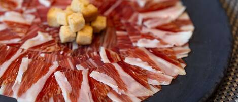 A circular arrangement of thinly sliced meat on a plate, with small cubes of a yellowish food item in the center.