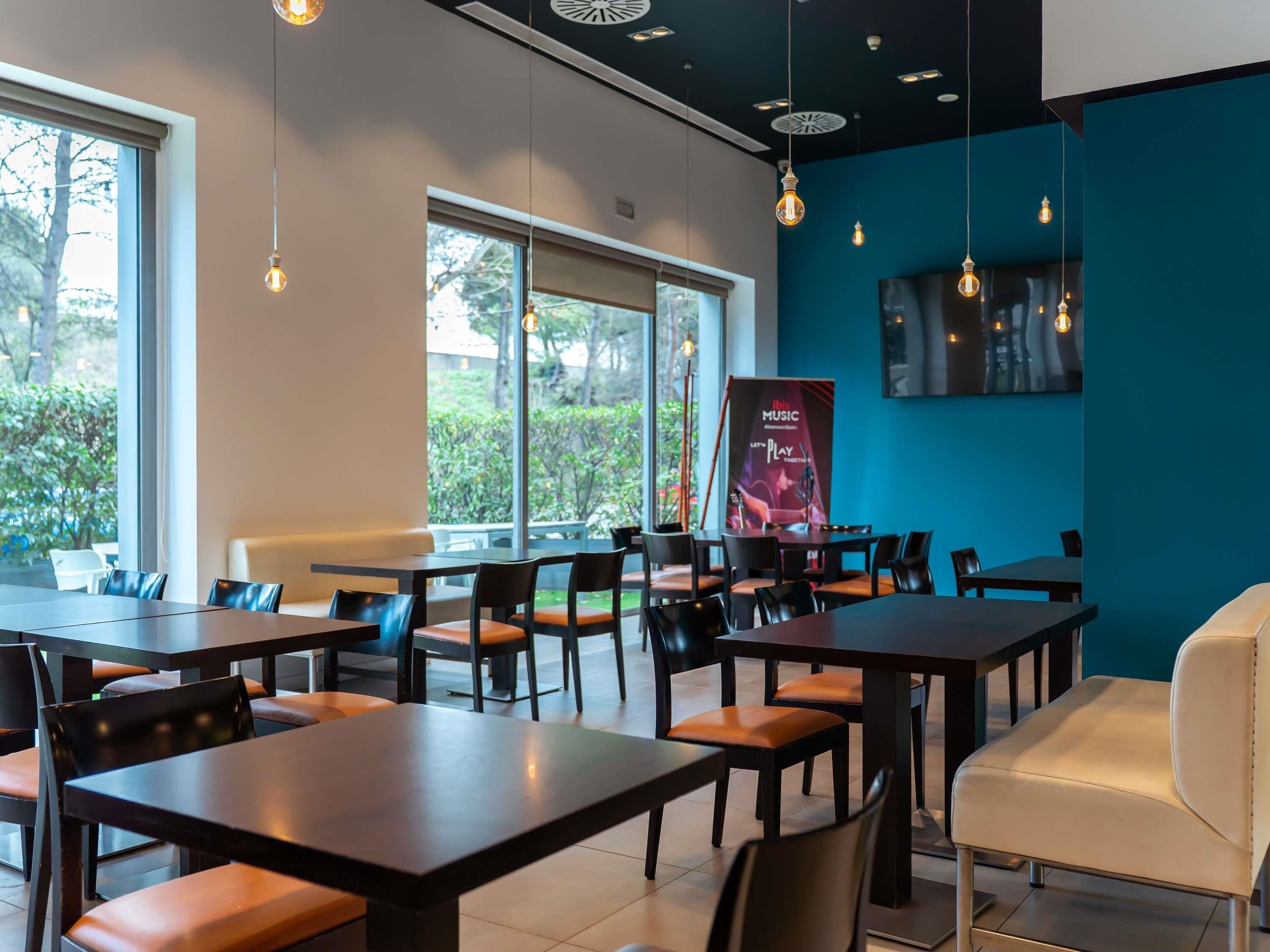 A restaurant interior with tables and chairs, large windows, and a blue accent wall.