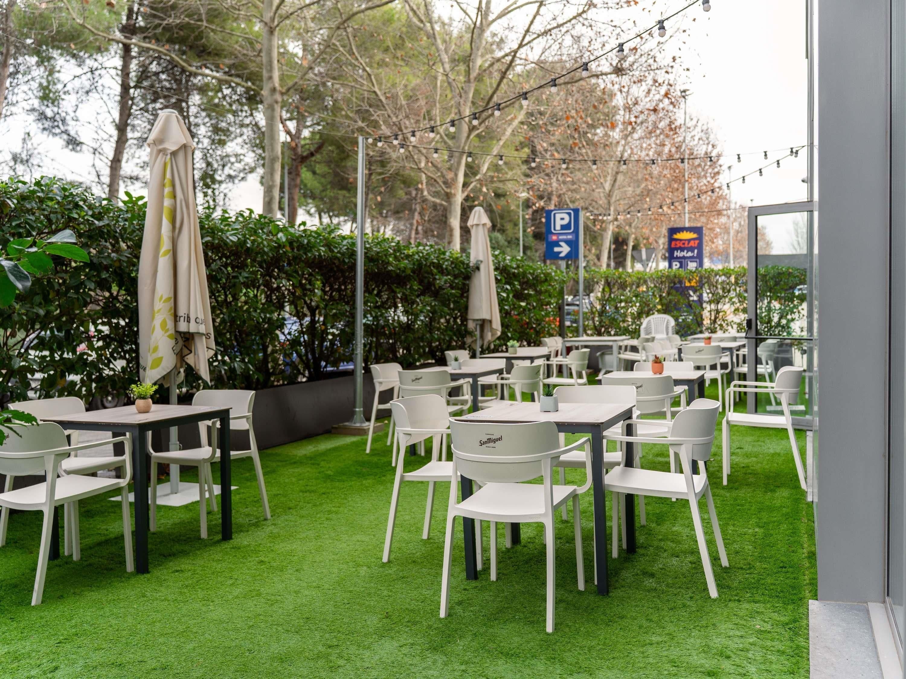 An outdoor seating area with tables and chairs, surrounded by greenery and trees.