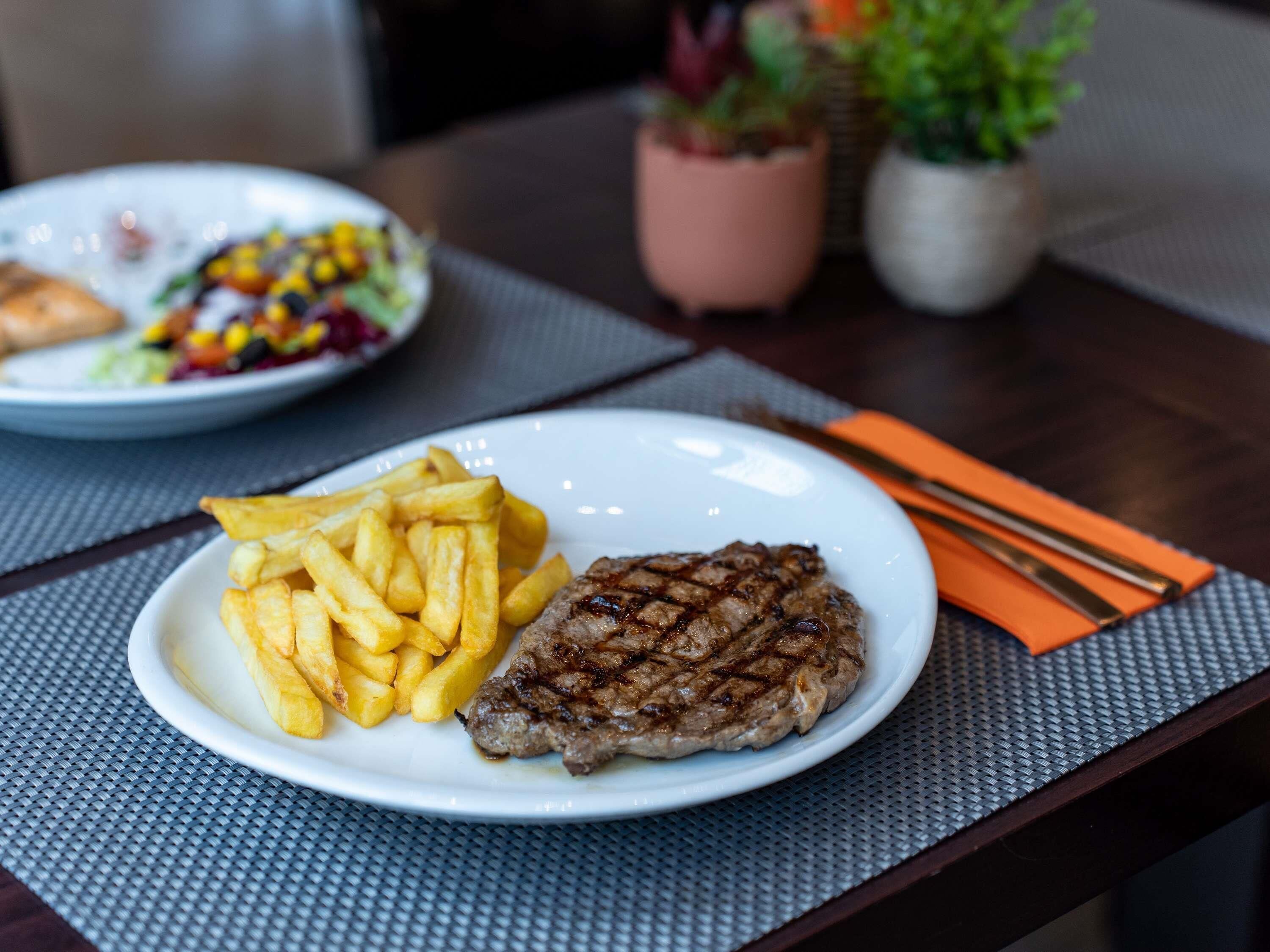 A plate with a grilled steak and fries on a table with a placemat.