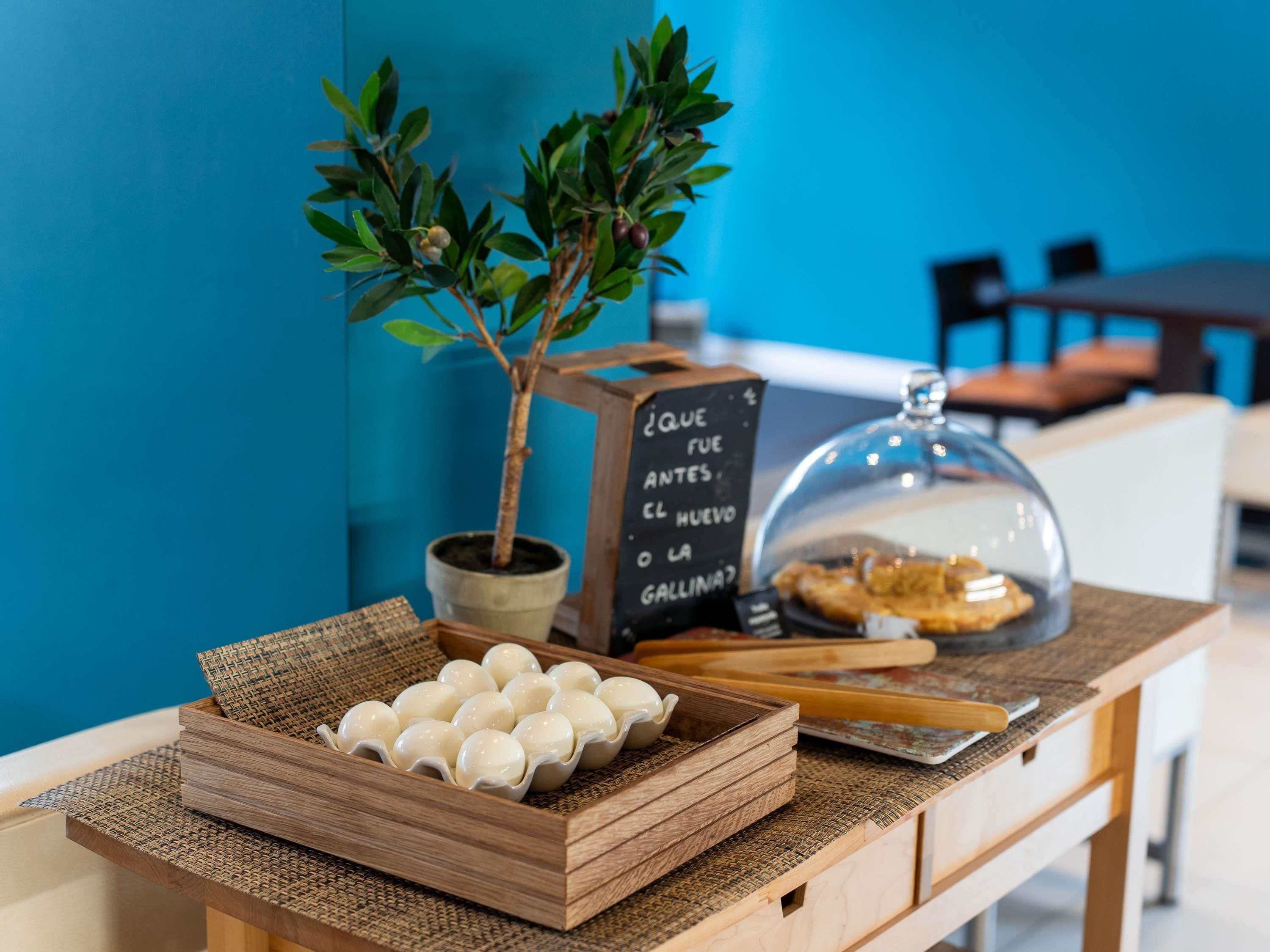 Una mesa con una planta, una pizarra con el menú y un recipiente tapado.