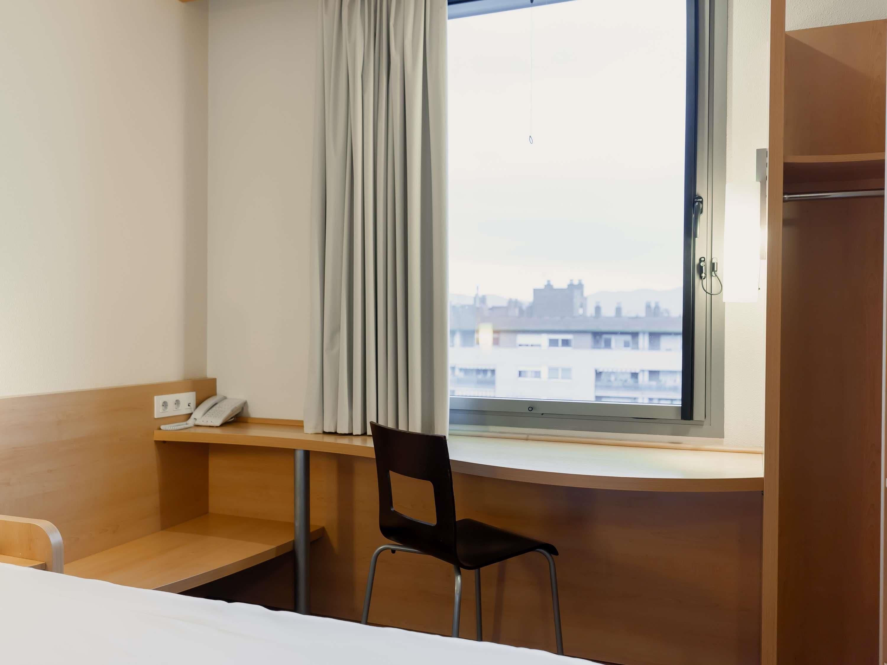 Une chambre d’hôtel équipée d’un bureau, d’une chaise et d’une fenêtre donnant sur des immeubles.