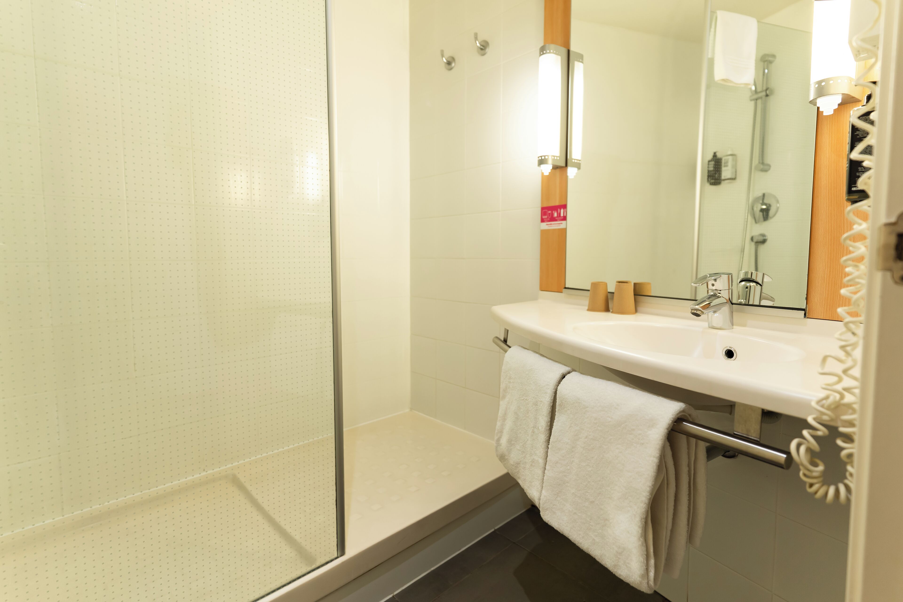 A bathroom with a glass shower enclosure, a sink with a mirror, and a towel rack.