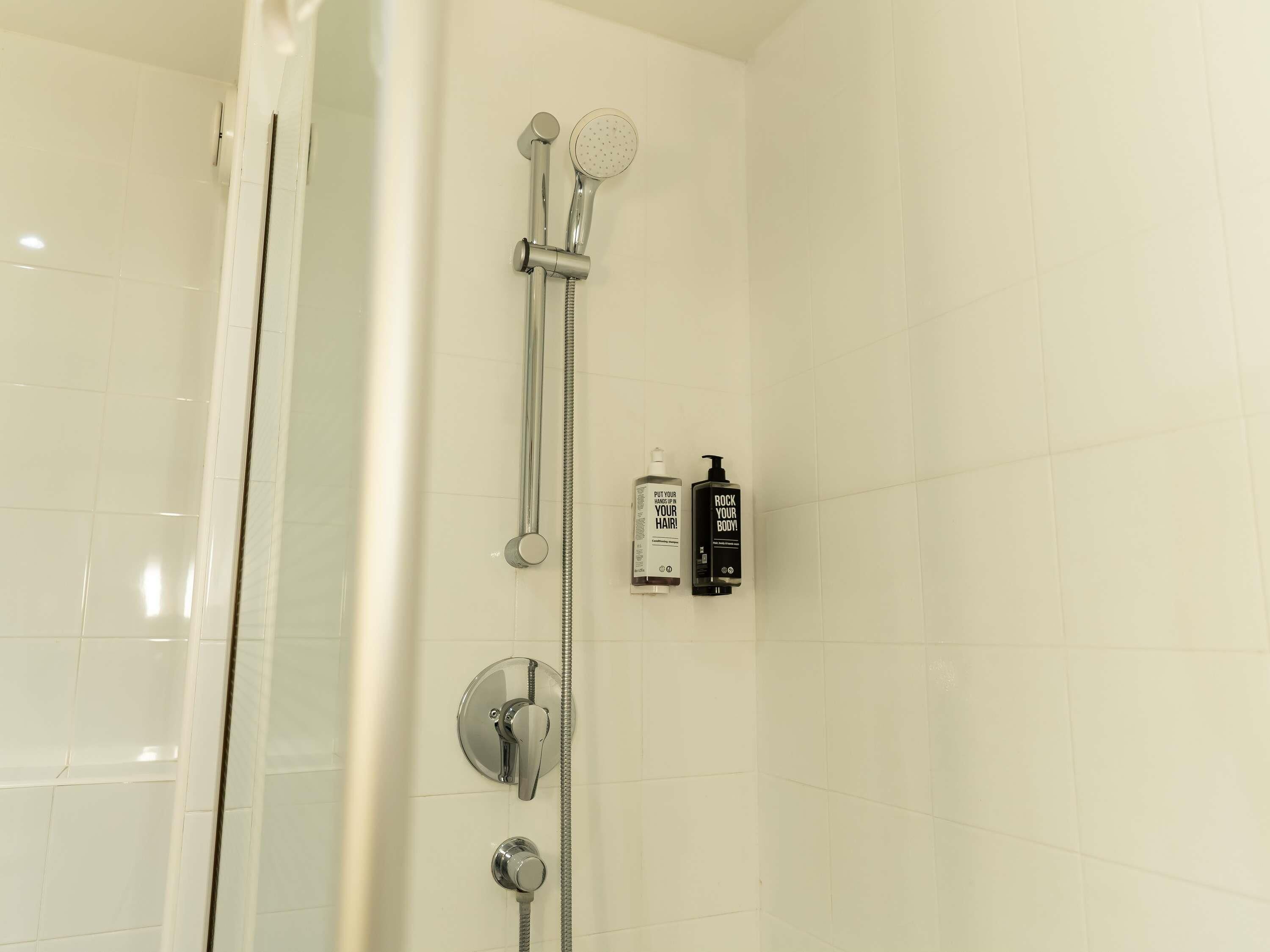 Una ducha con cabezal de ducha de mano, grifo empotrado en la pared y cabezal de ducha manual. Hay dos botellas de champú y acondicionador en la pared.