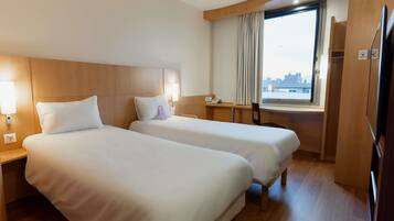 A hotel room with two beds, a desk, a chair, a window with curtains, and a city view.