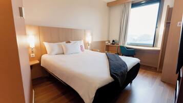 A hotel room with a large bed, bedside lamps, a desk, a chair, and a window with curtains.