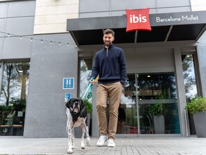 A man walking a dog in front of a building with a sign that reads 'ibis Barcelona Mollet.' - ibis Barcelona Mollet (Mollet del Valles)