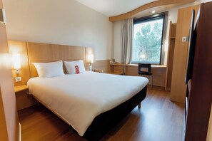 Habitación de hotel con una cama grande, lámparas de noche, un escritorio, una silla, un ventanal con cortinas y un televisor.