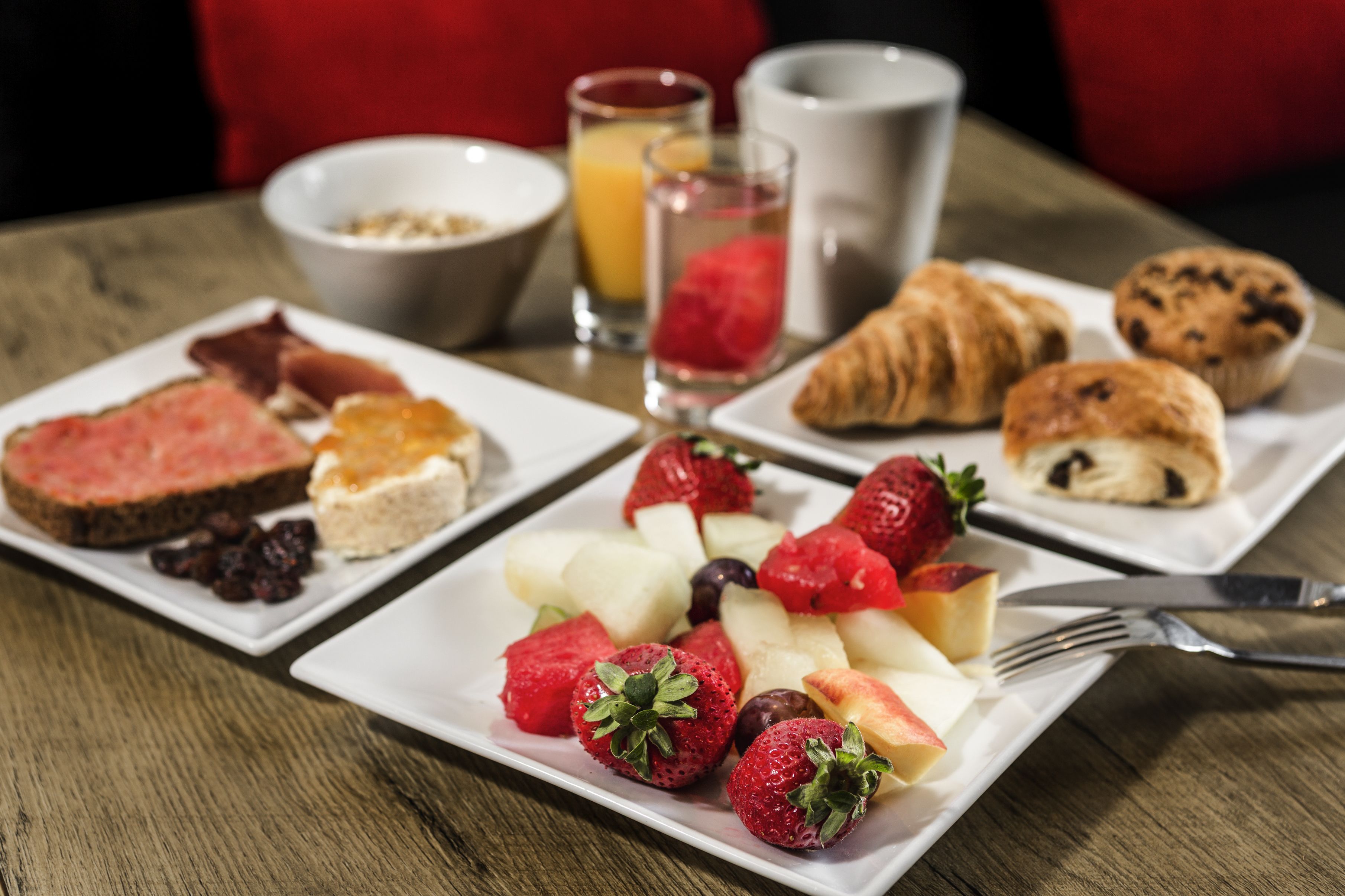 Une table mise pour le petit-déjeuner avec des assiettes de toasts, des fruits, des croissants et un verre de jus d’orange.