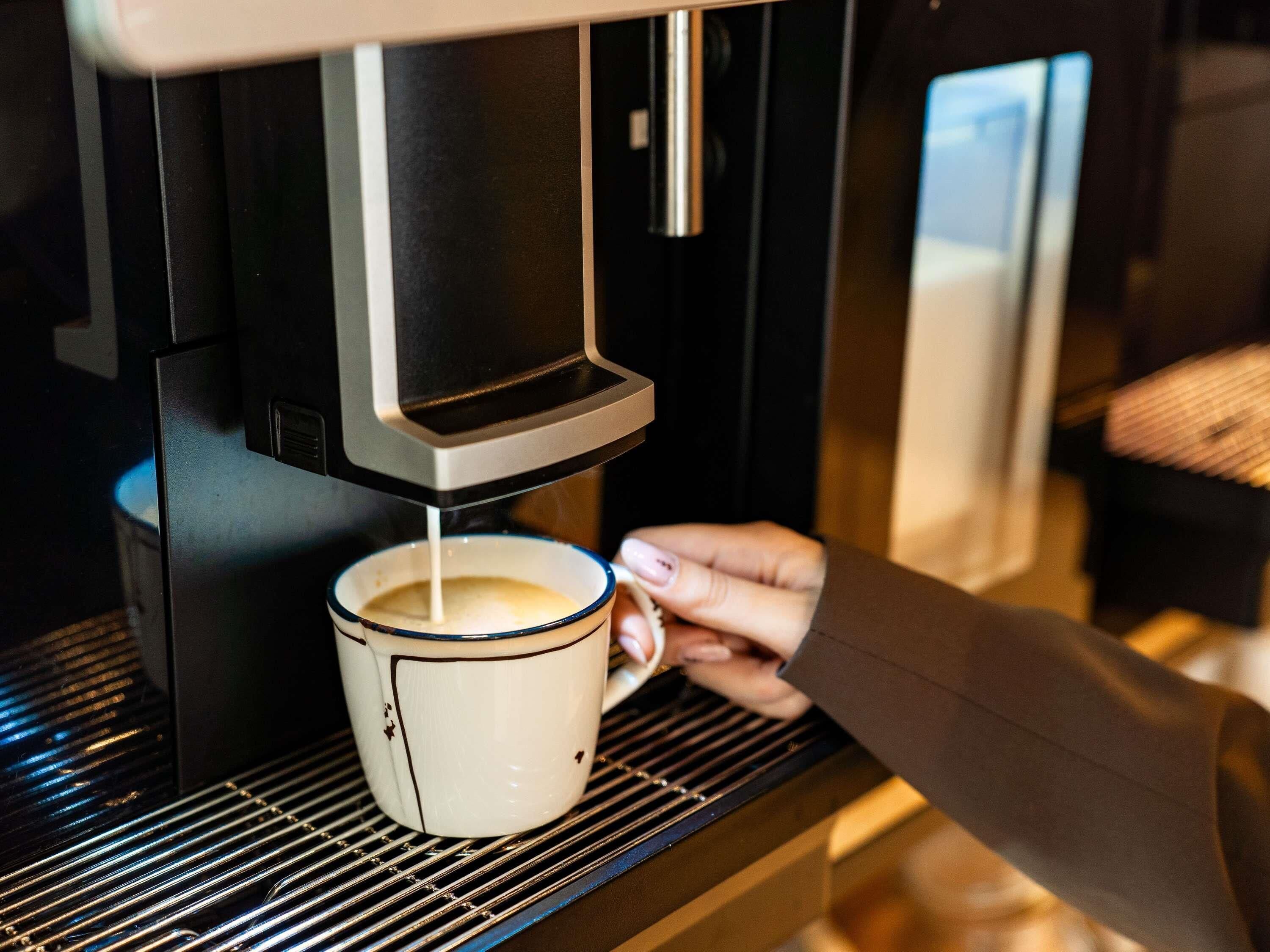 En hand håller i en mugg under en kaffemaskin.