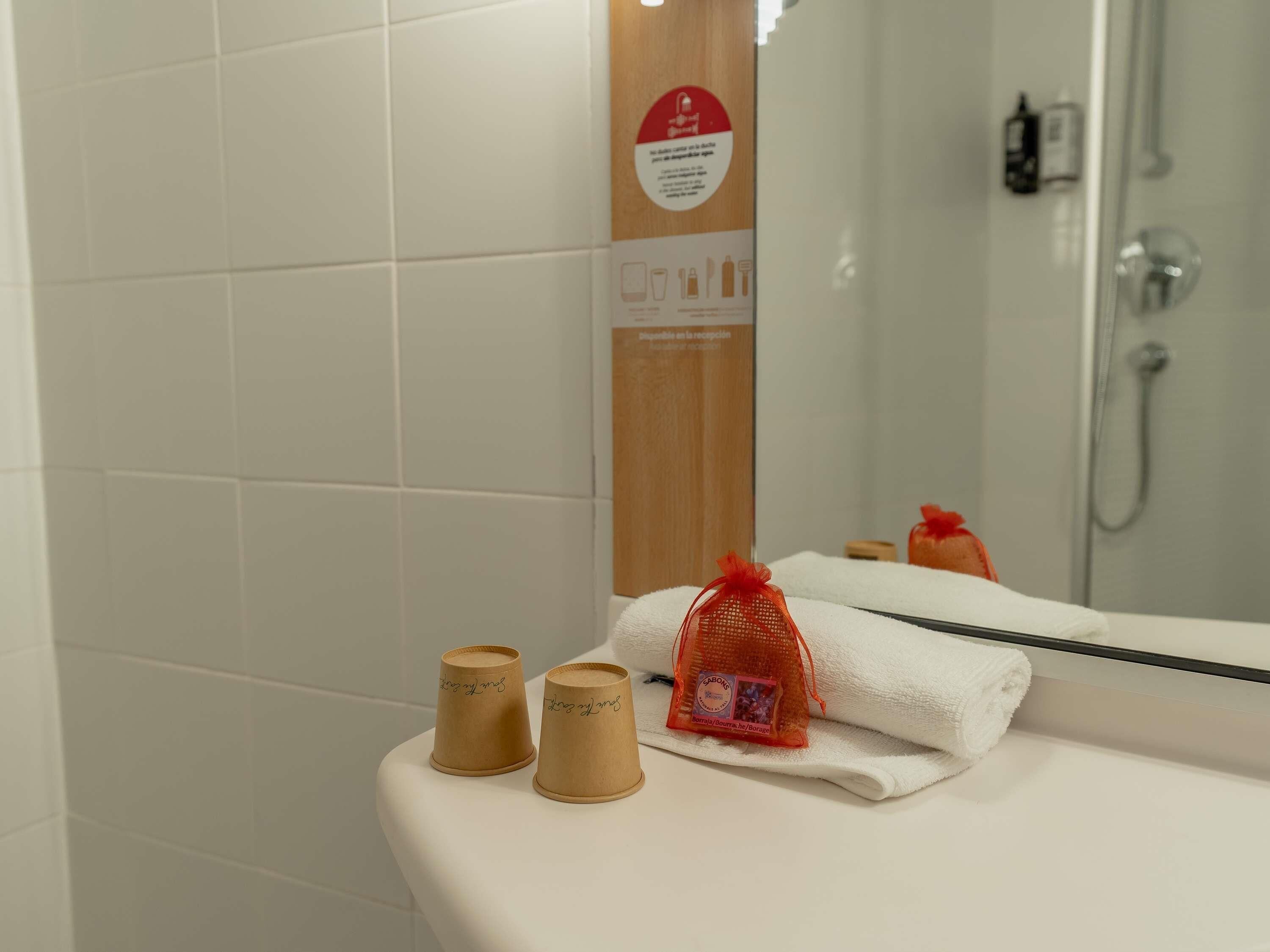 Un baño con azulejos blancos, un espejo, una ducha y un perchero para toallas.