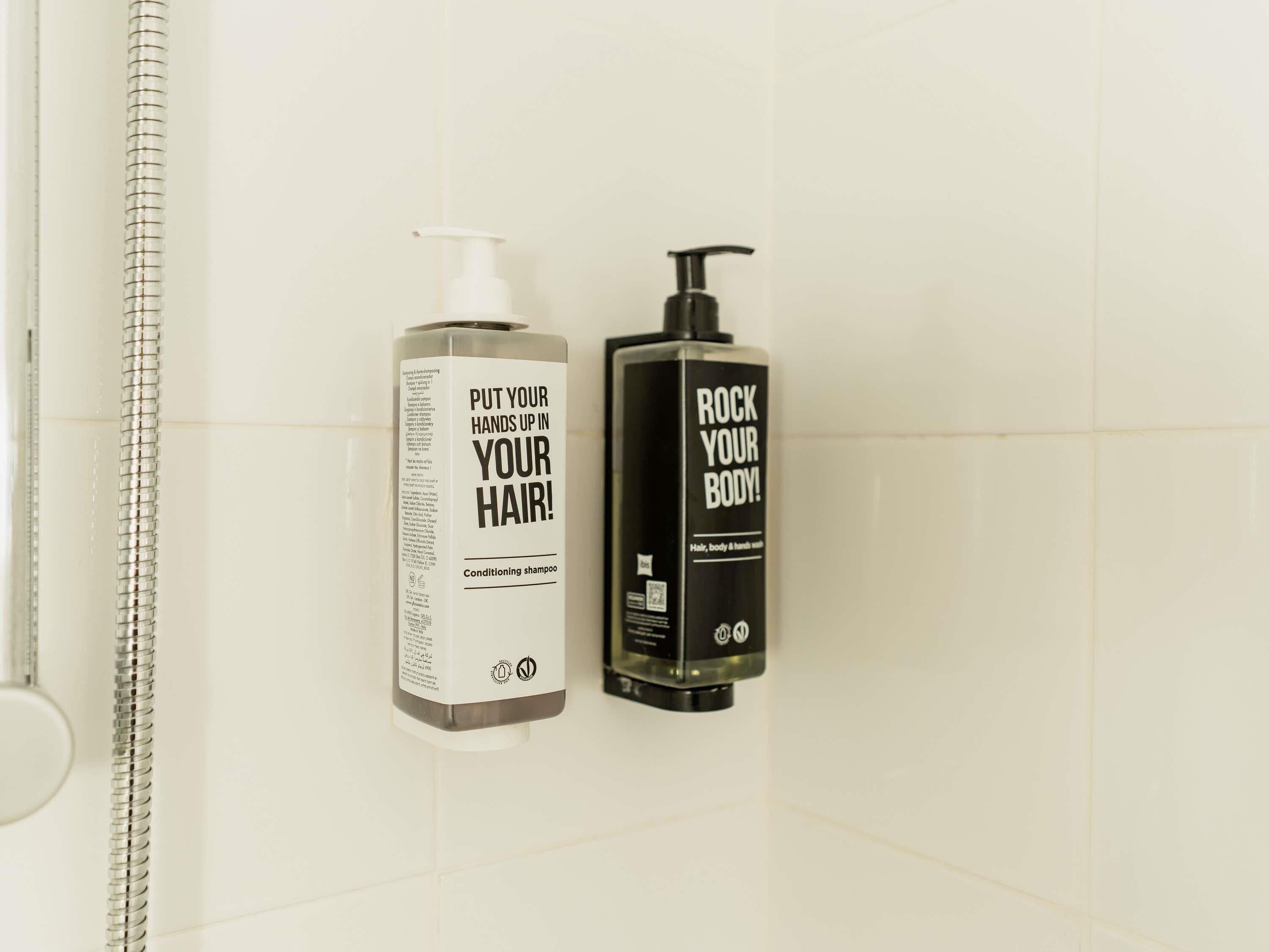 Two bottles of shampoo on a tiled wall.