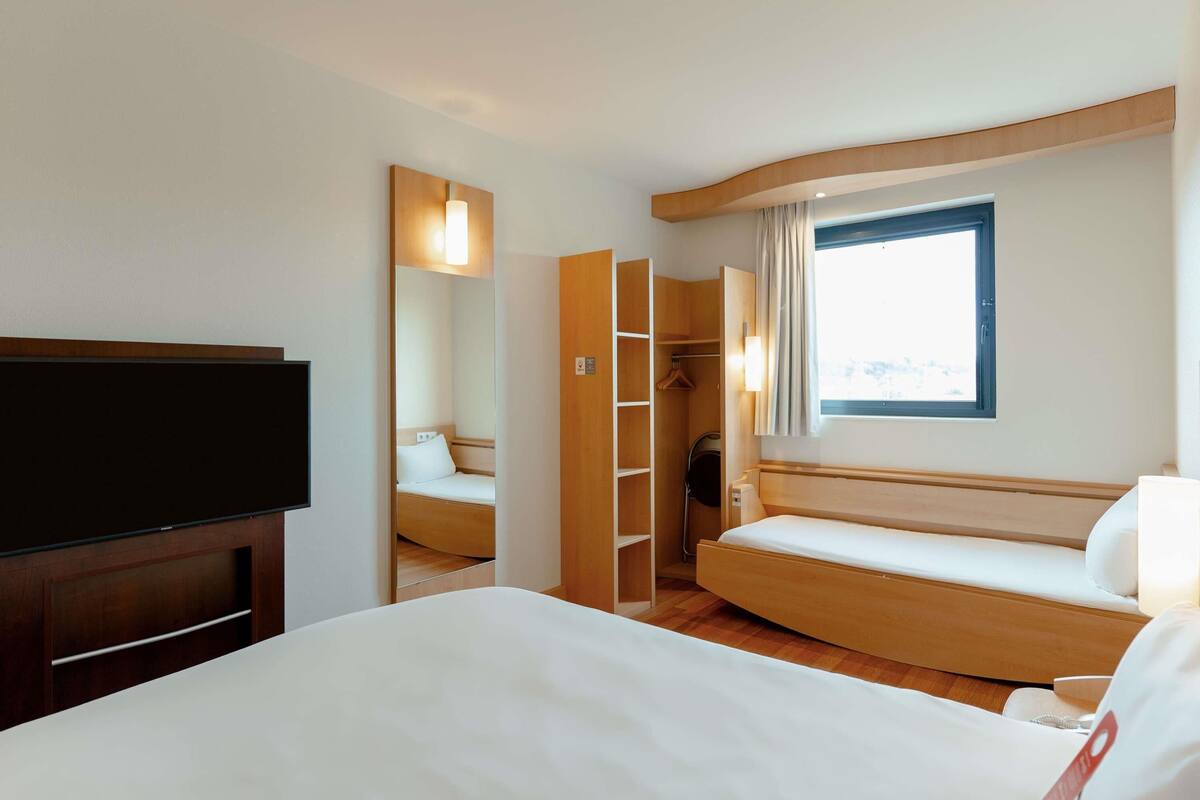 A hotel room with a bed, a TV, a wardrobe, and a window.