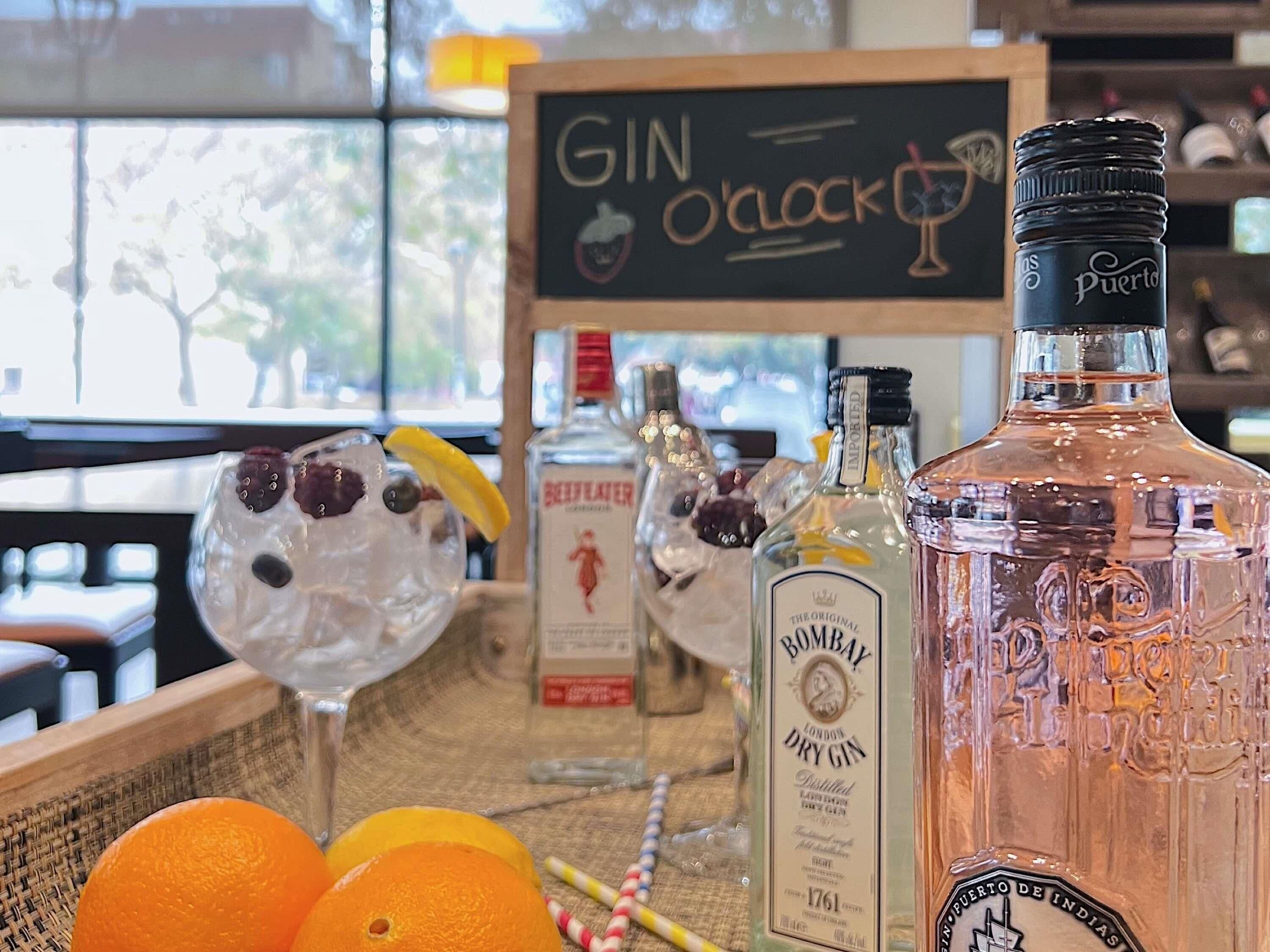 Eine Bar mit einer Beschilderung für Gin o'clock, Flaschen Bombay Dry Gin und eine Flasche Puerto de Indias.