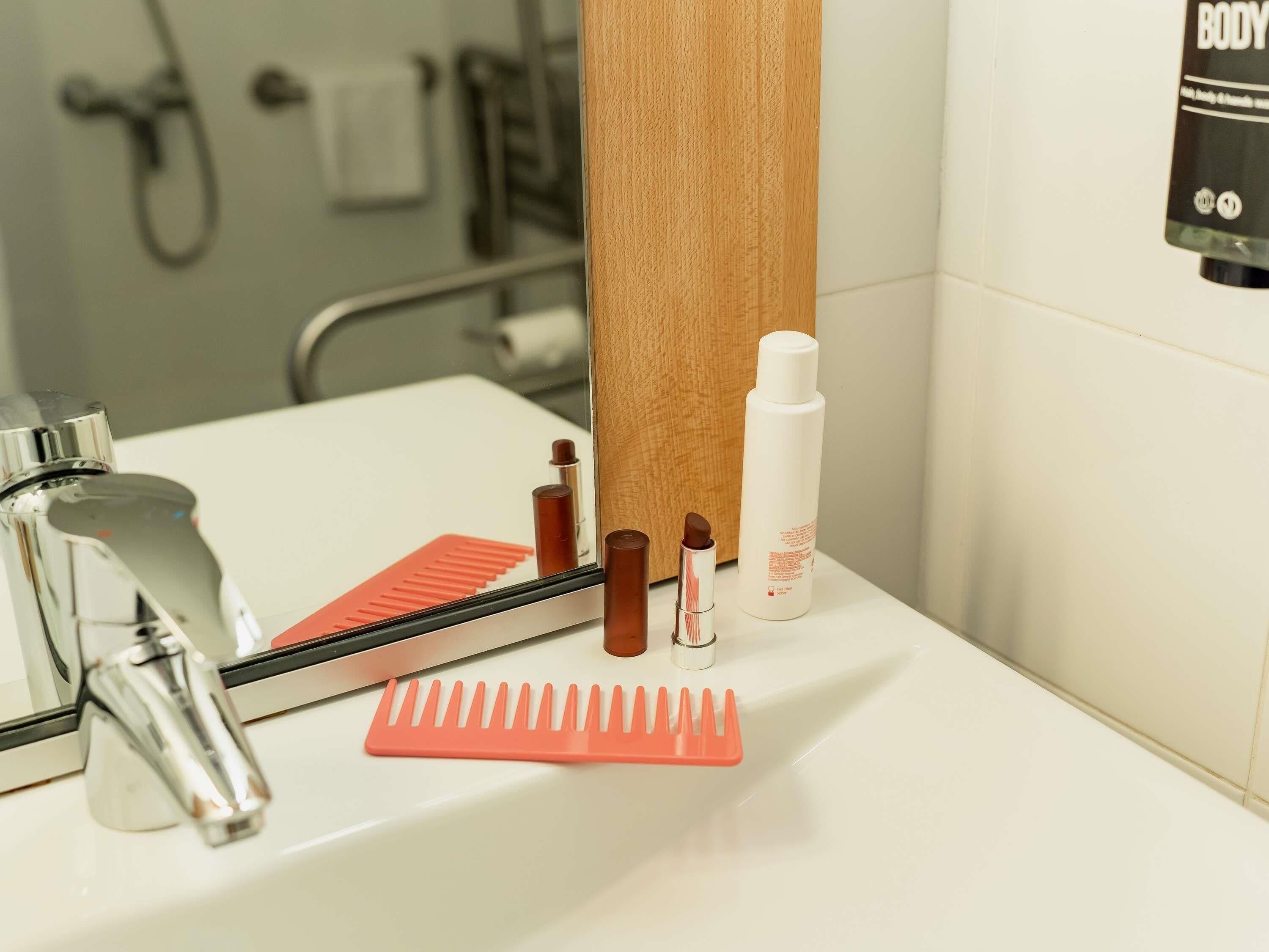 Un lavabo de salle de bain avec un miroir, un robinet, un peigne et un flacon de lotion.